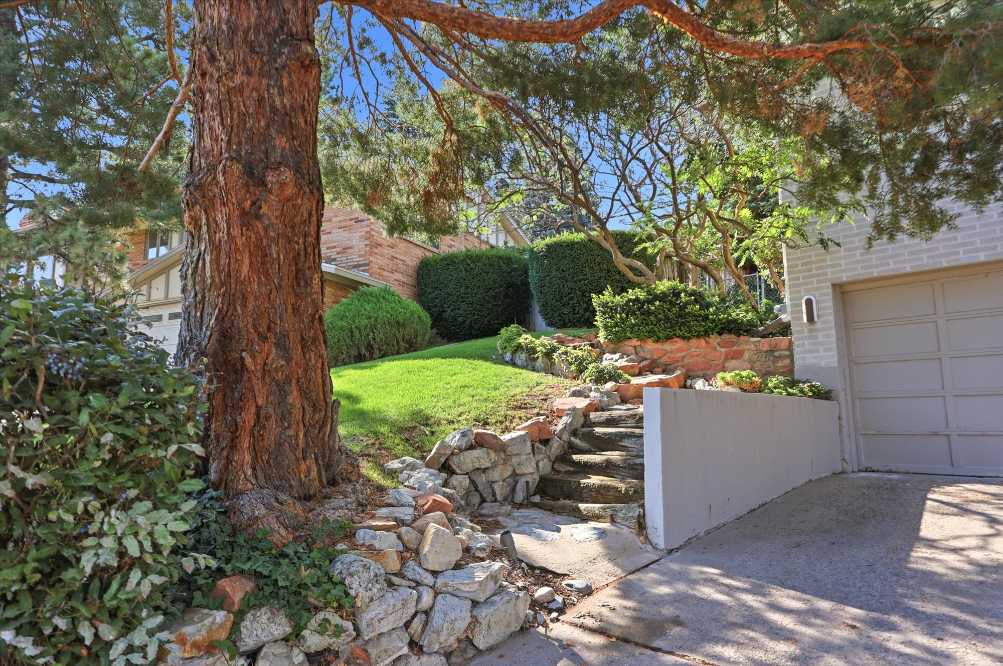 Mature trees frame a landscaped front yard featuring stone retaining walls and steps