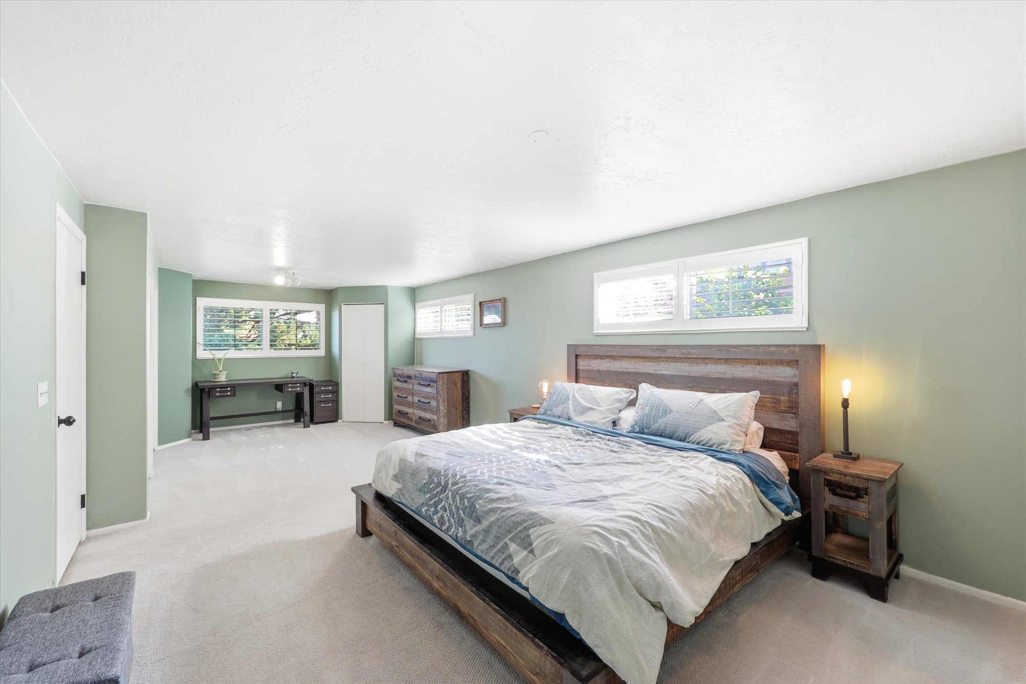 Spacious room featuring light green walls, white trim, light-colored carpeting, multiple windows with blinds, and white doors