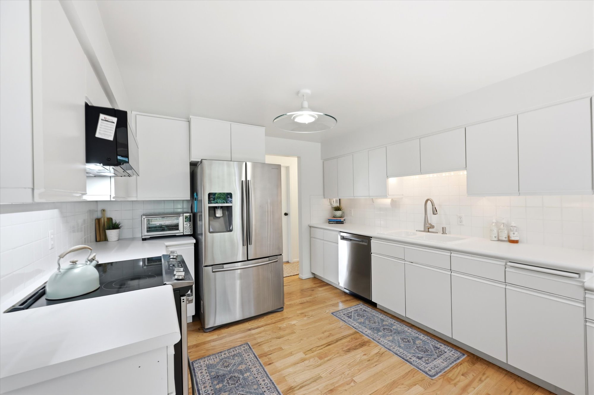 Bright kitchen featuring extensive white cabinetry, light countertops, wood-finish flooring, a white subway tile backsplash, and stainless steel appliances