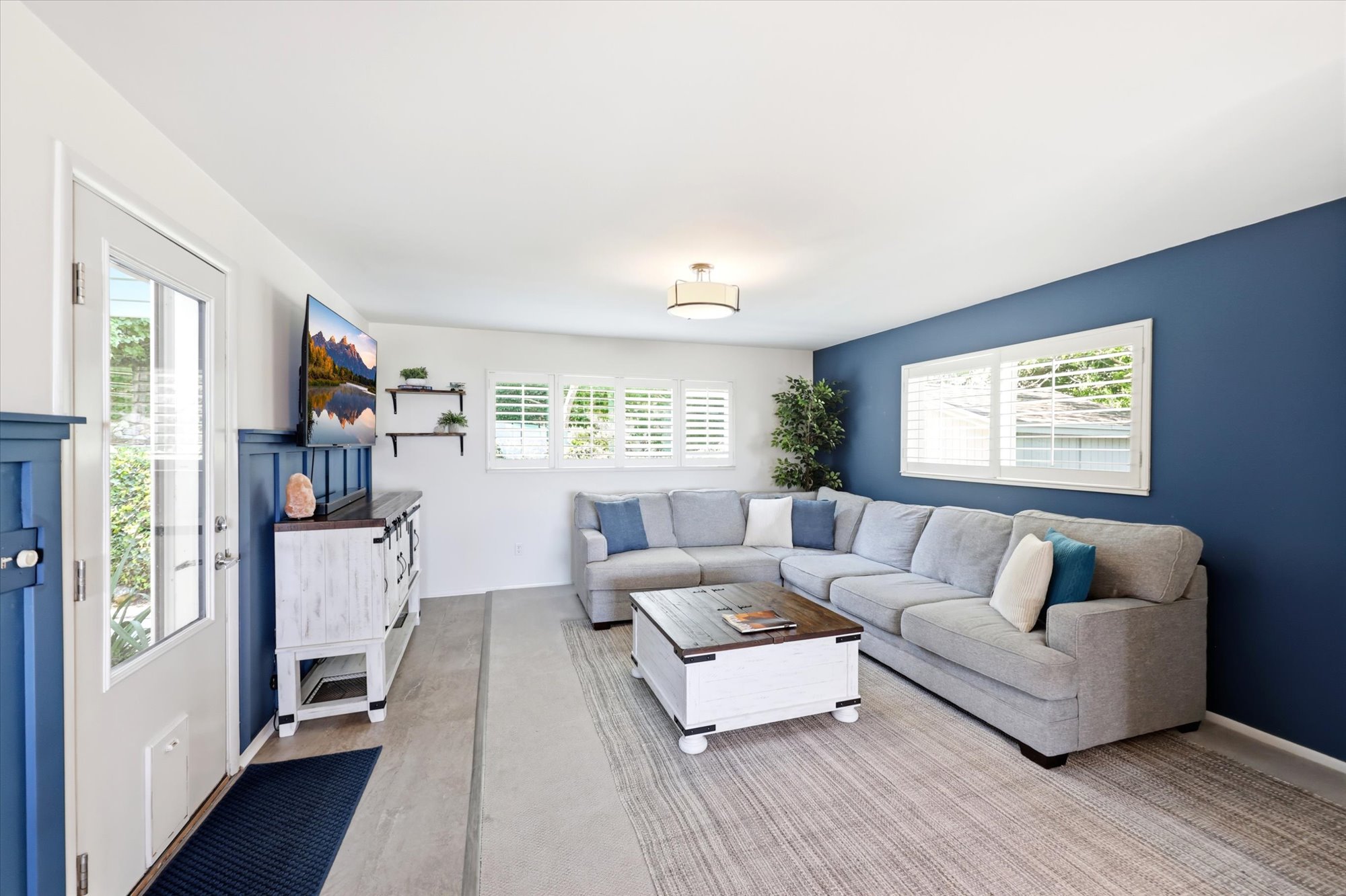 Spacious living area featuring a prominent accent wall, multiple windows with white plantation shutters, and light wood-finish flooring
