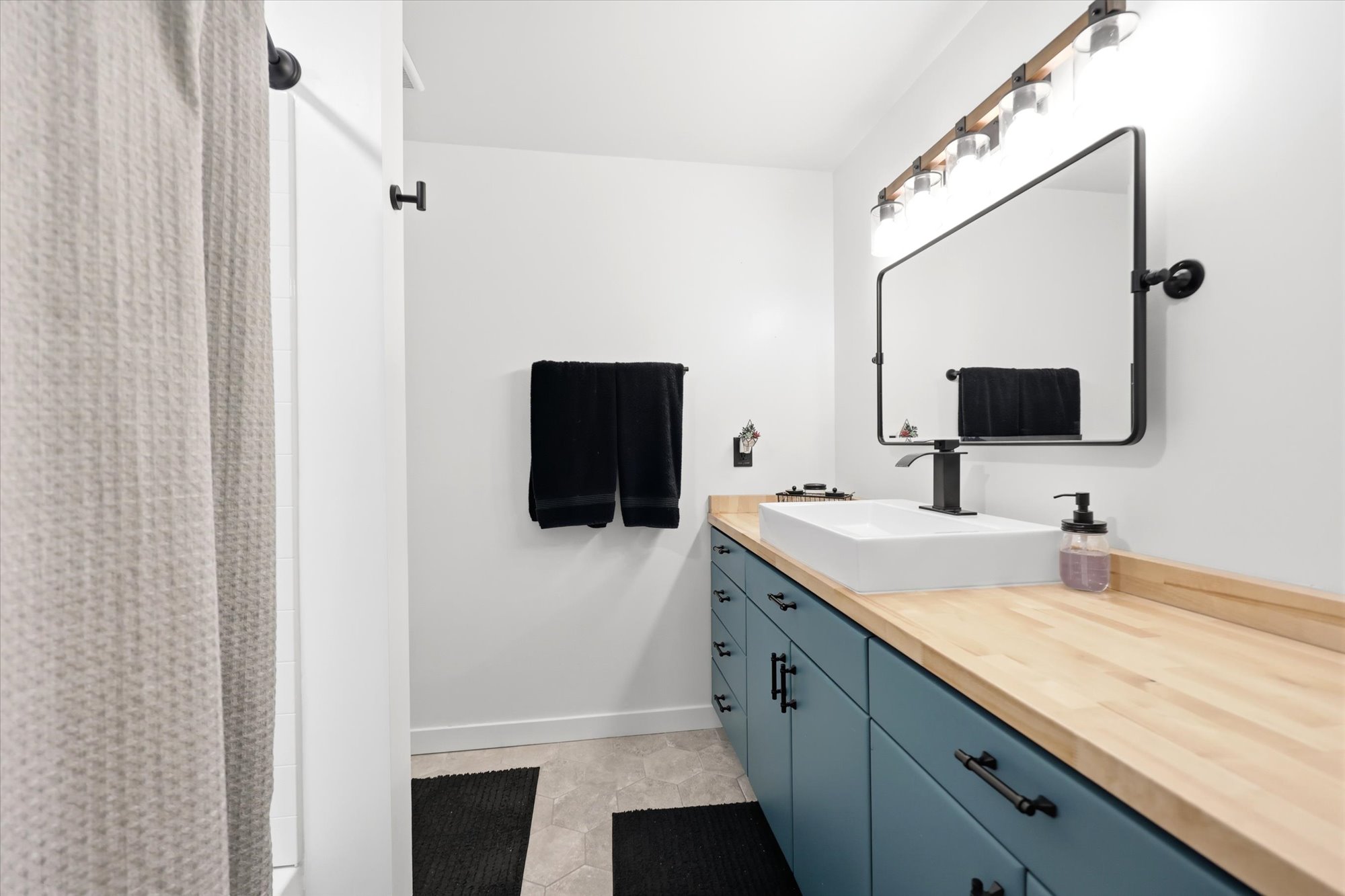 Bathroom featuring a vessel sink, wood-finish countertop, and a wall-mounted rectangular mirror