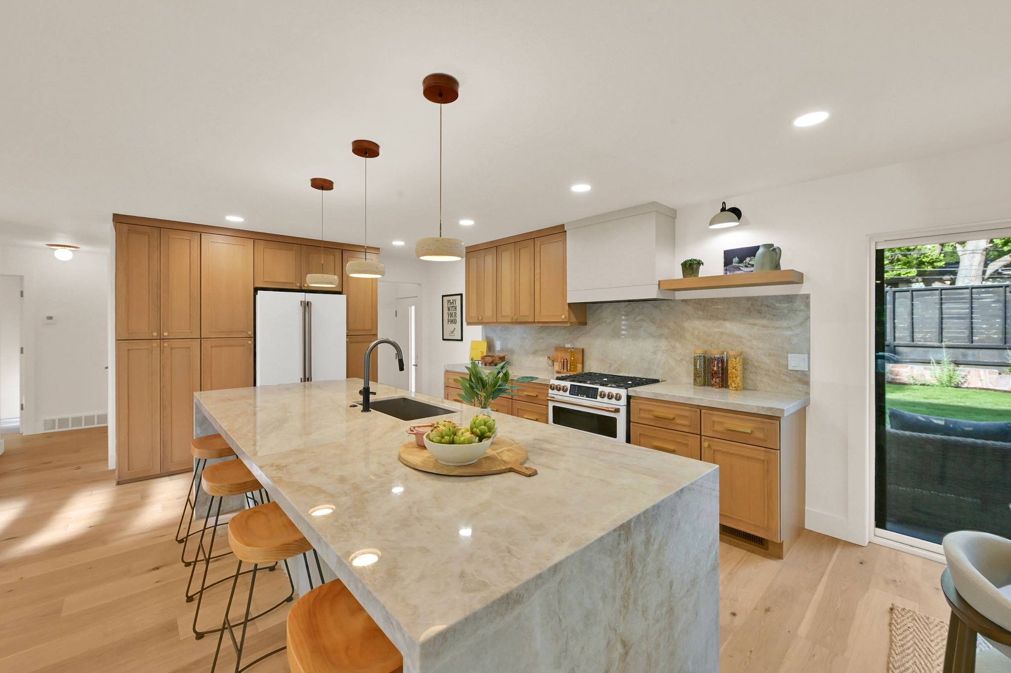 Spacious kitchen featuring an oversized island with countertop seating, a matte black faucet with an undermount sink, and a full-height stone backsplash