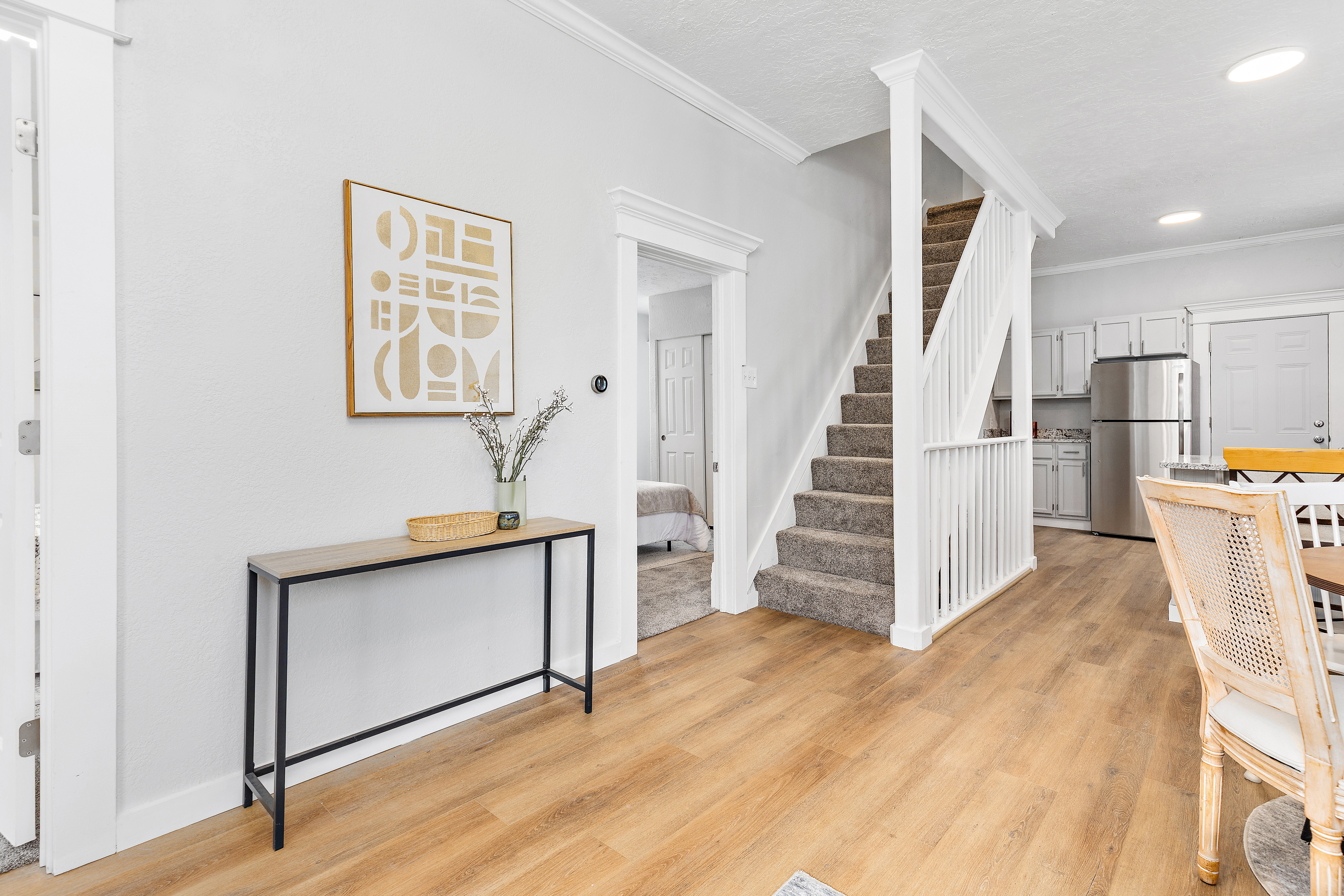 Open-concept living space featuring wood-finish flooring, a carpeted staircase with white balusters, and crown molding