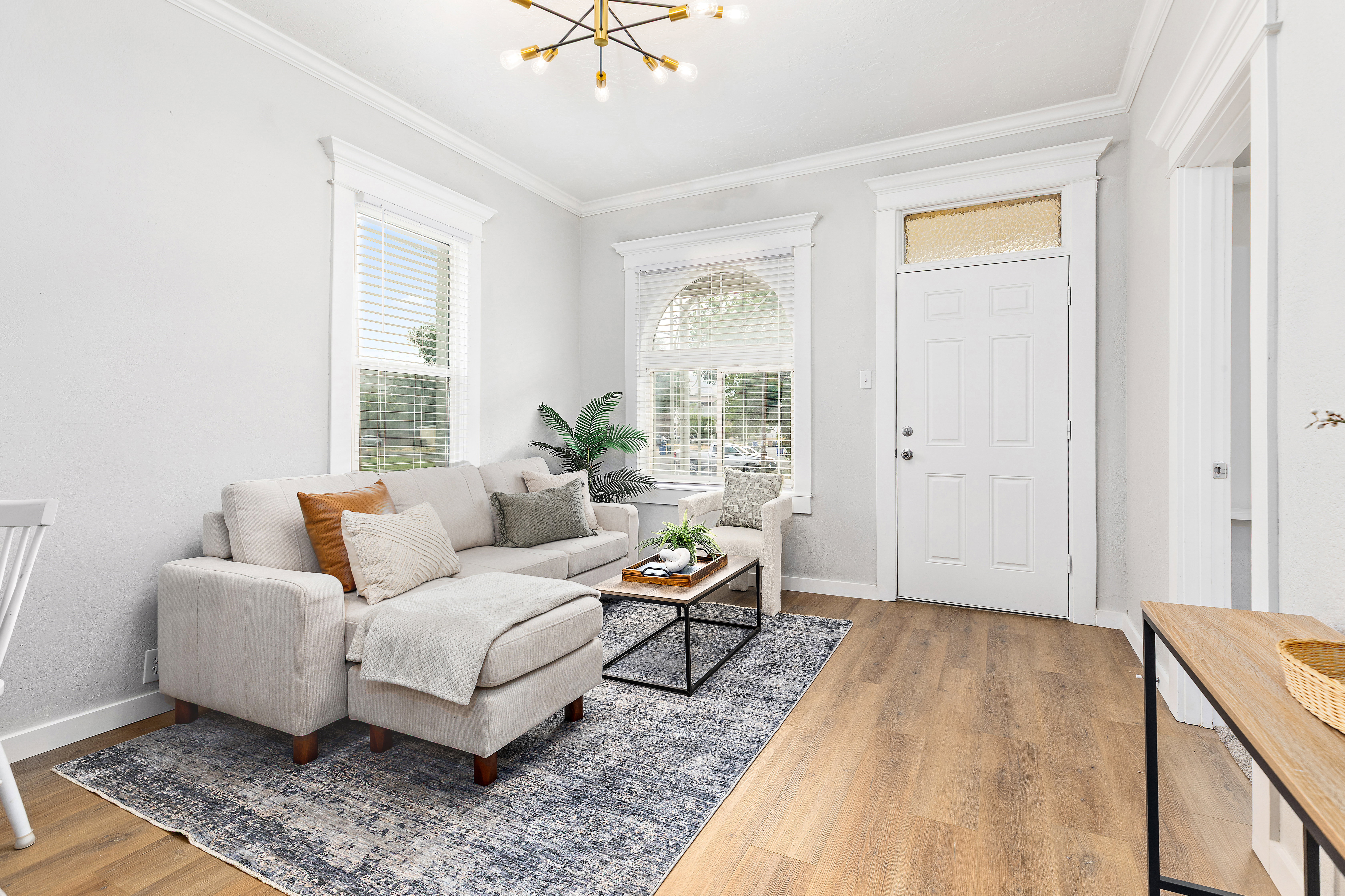 Living area featuring wood-finish flooring, a contemporary chandelier, white trim, and a prominent entry door with a transom window