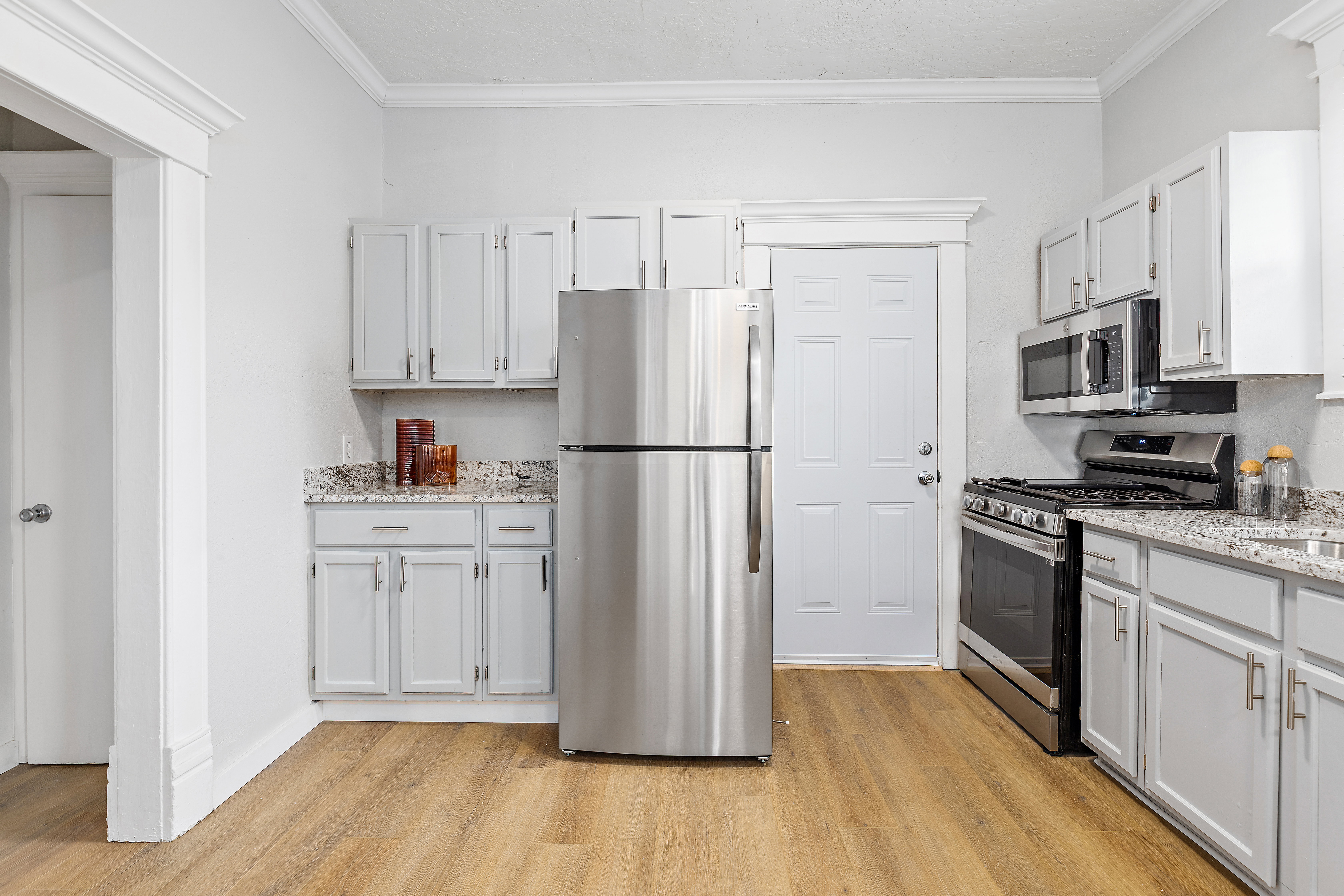 Kitchen featuring light gray cabinetry, stainless steel appliances, speckled countertops, and wood-finish flooring