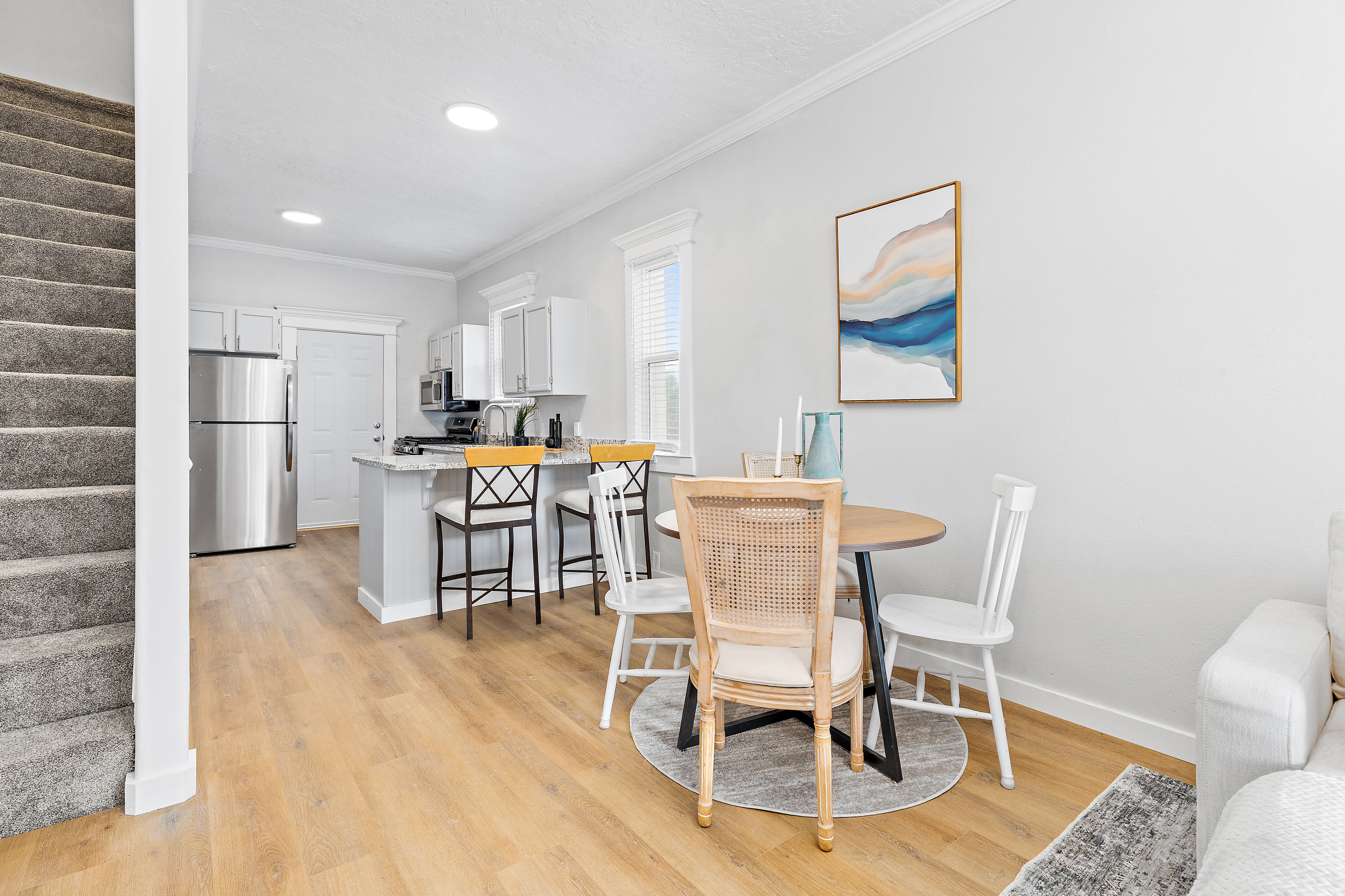 Open-concept living space with wood-finish flooring, a kitchen featuring stainless steel appliances, and a carpeted staircase