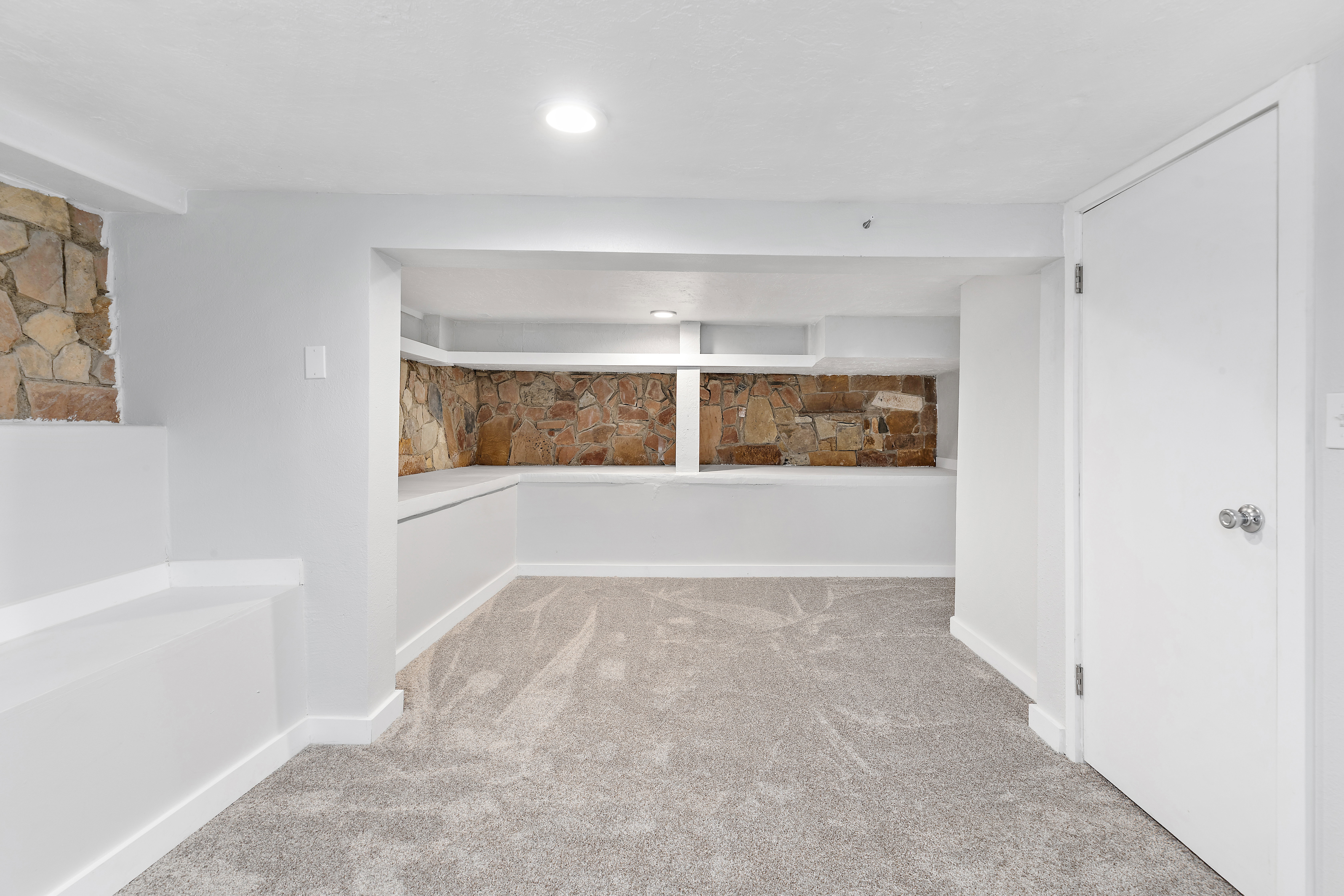 Carpeted interior space featuring white walls and a stone accent wall with built-in shelving