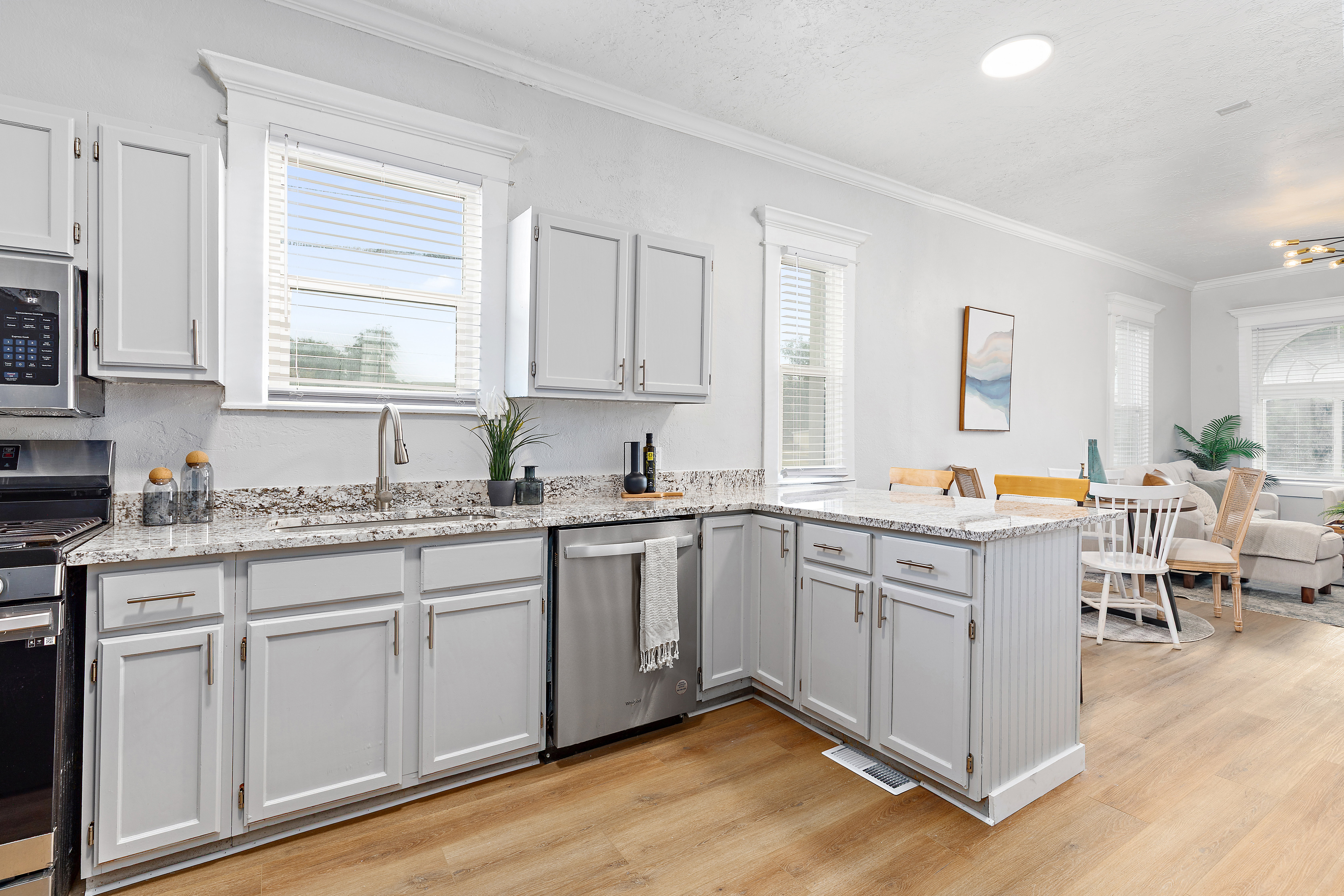 Bright kitchen featuring light-toned cabinetry, granite-style countertops, stainless steel appliances, a built-in kitchen island, and wood-finish flooring