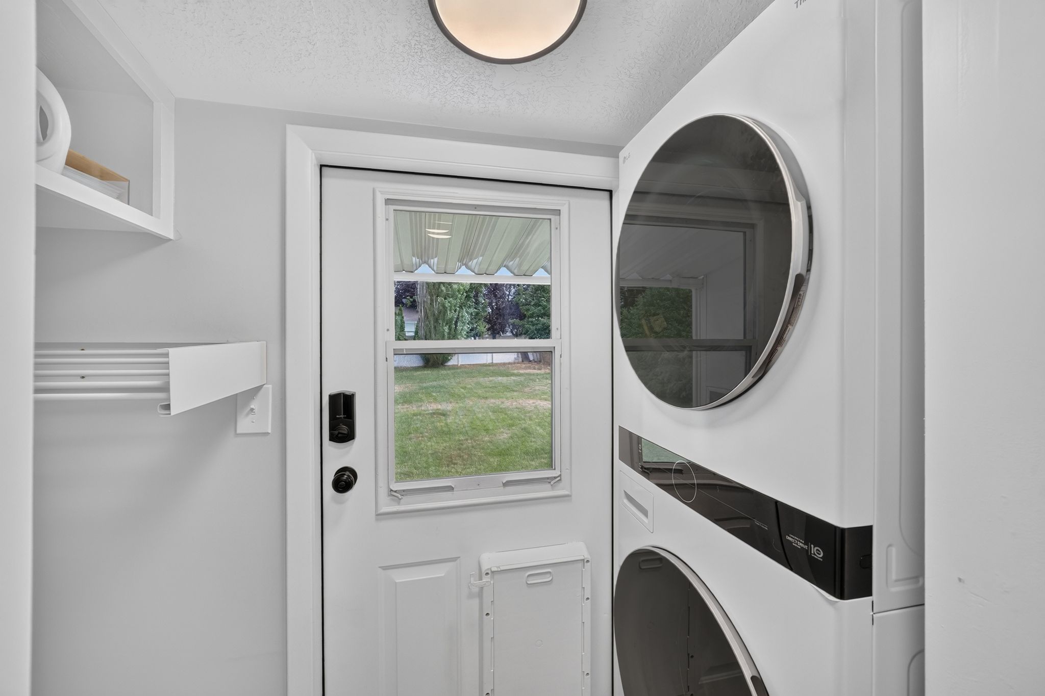 Dedicated laundry area featuring a stacked washer and dryer unit, built-in shelving, and a bright overhead light fixture