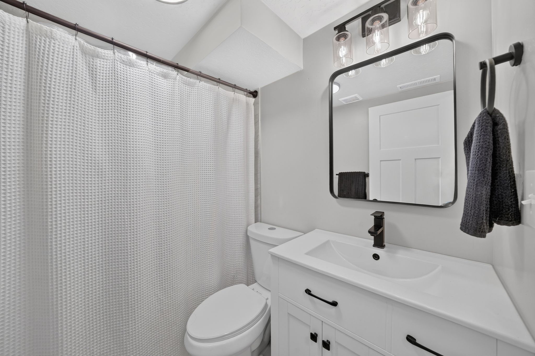 Bathroom featuring a white vanity with integrated sink, black hardware, framed mirror, three-light vanity fixture, and recessed lighting