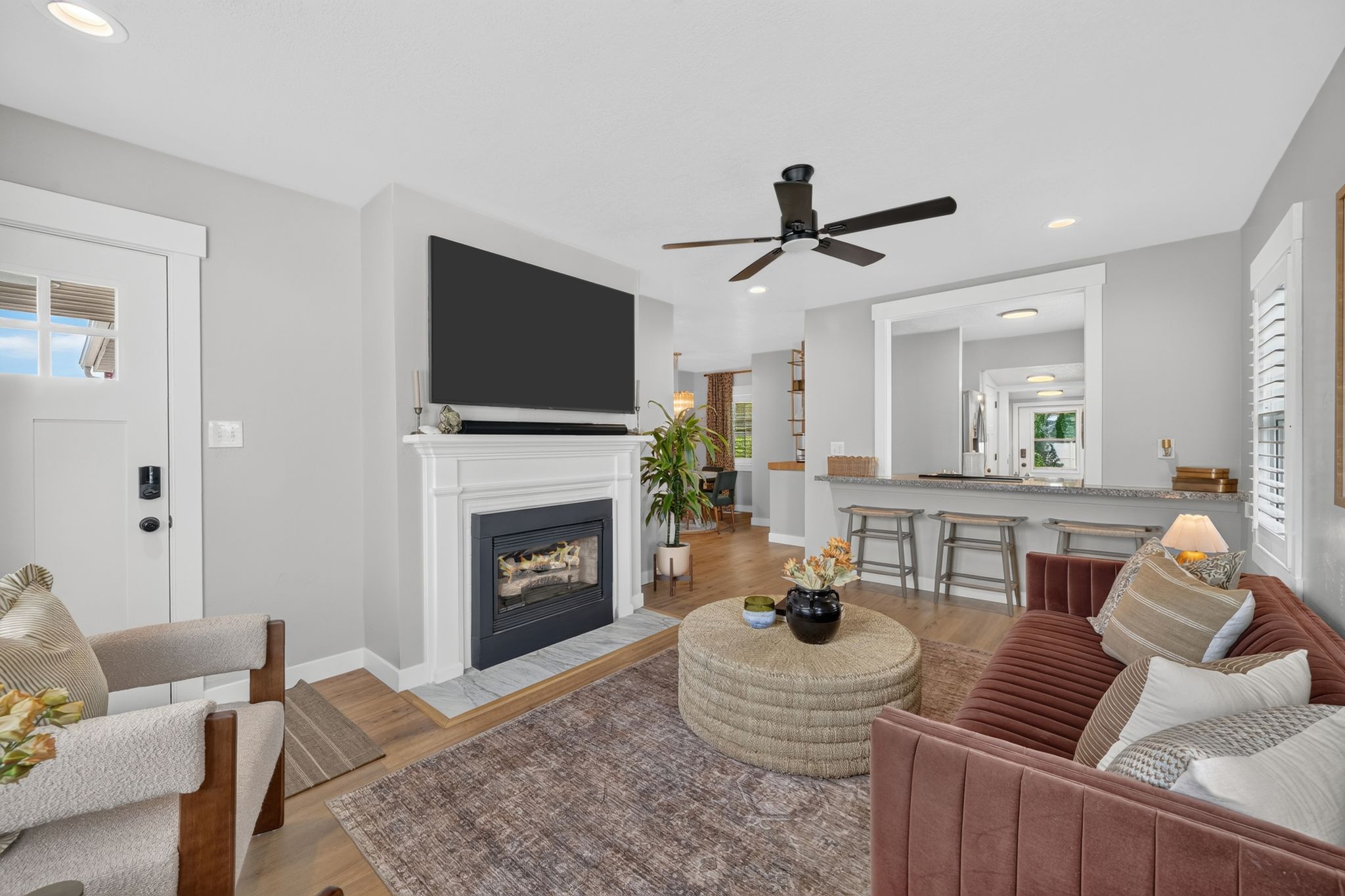 Living area featuring a classic fireplace with a white mantel, wood-finish flooring, and a ceiling fan