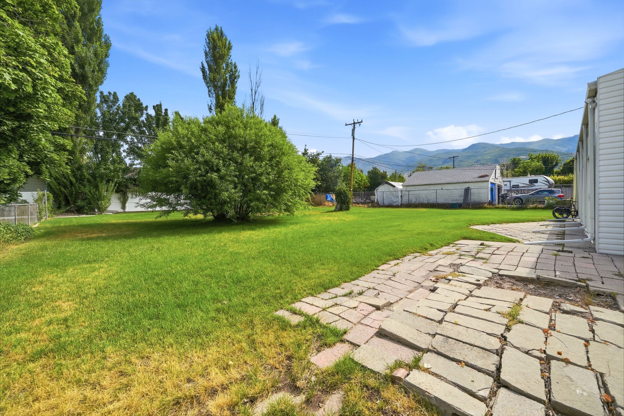 Expansive lawn area featuring mature trees and a stone patio