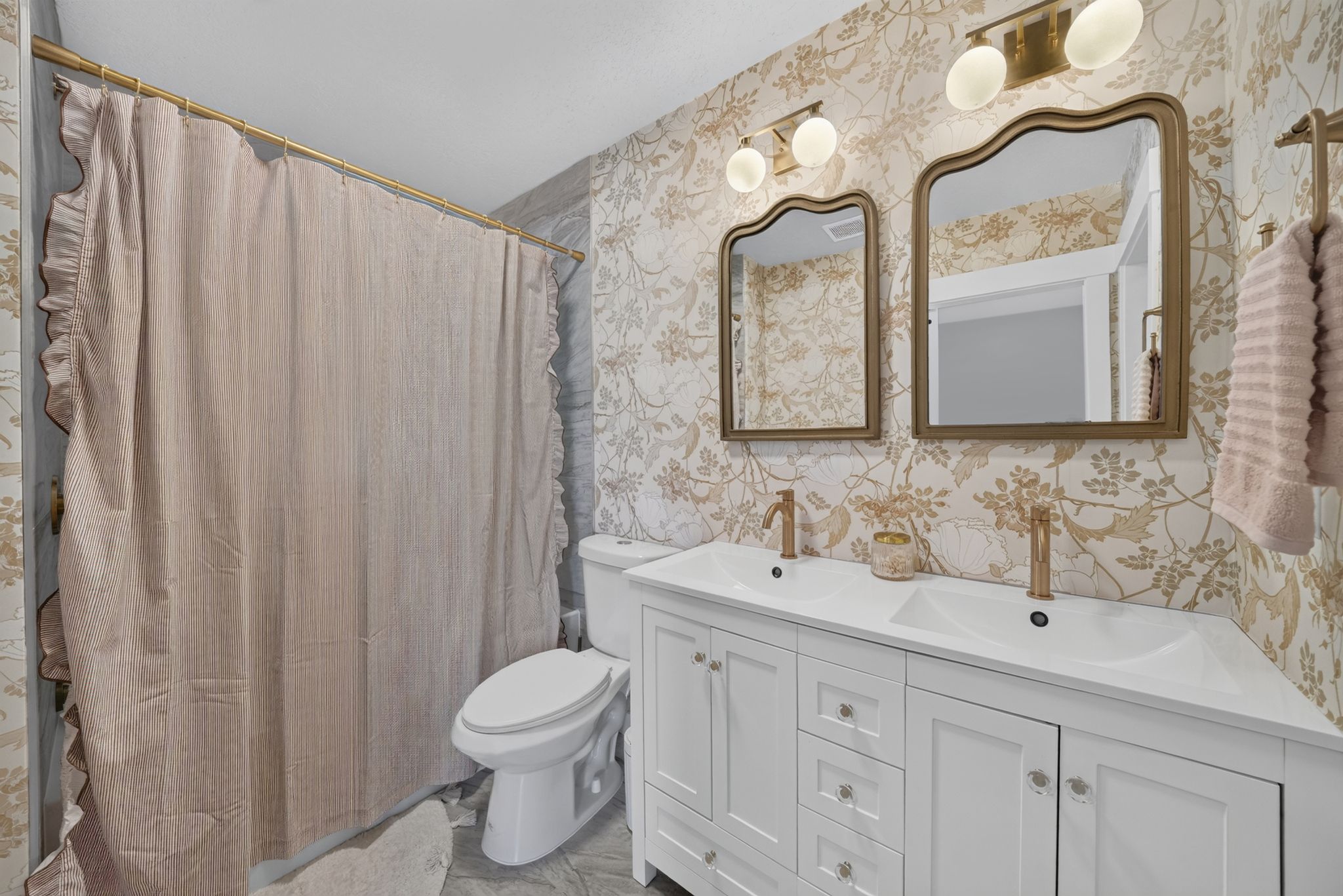 Bathroom featuring a dual vanity with white cabinetry, white integrated sinks, and brass-tone fixtures