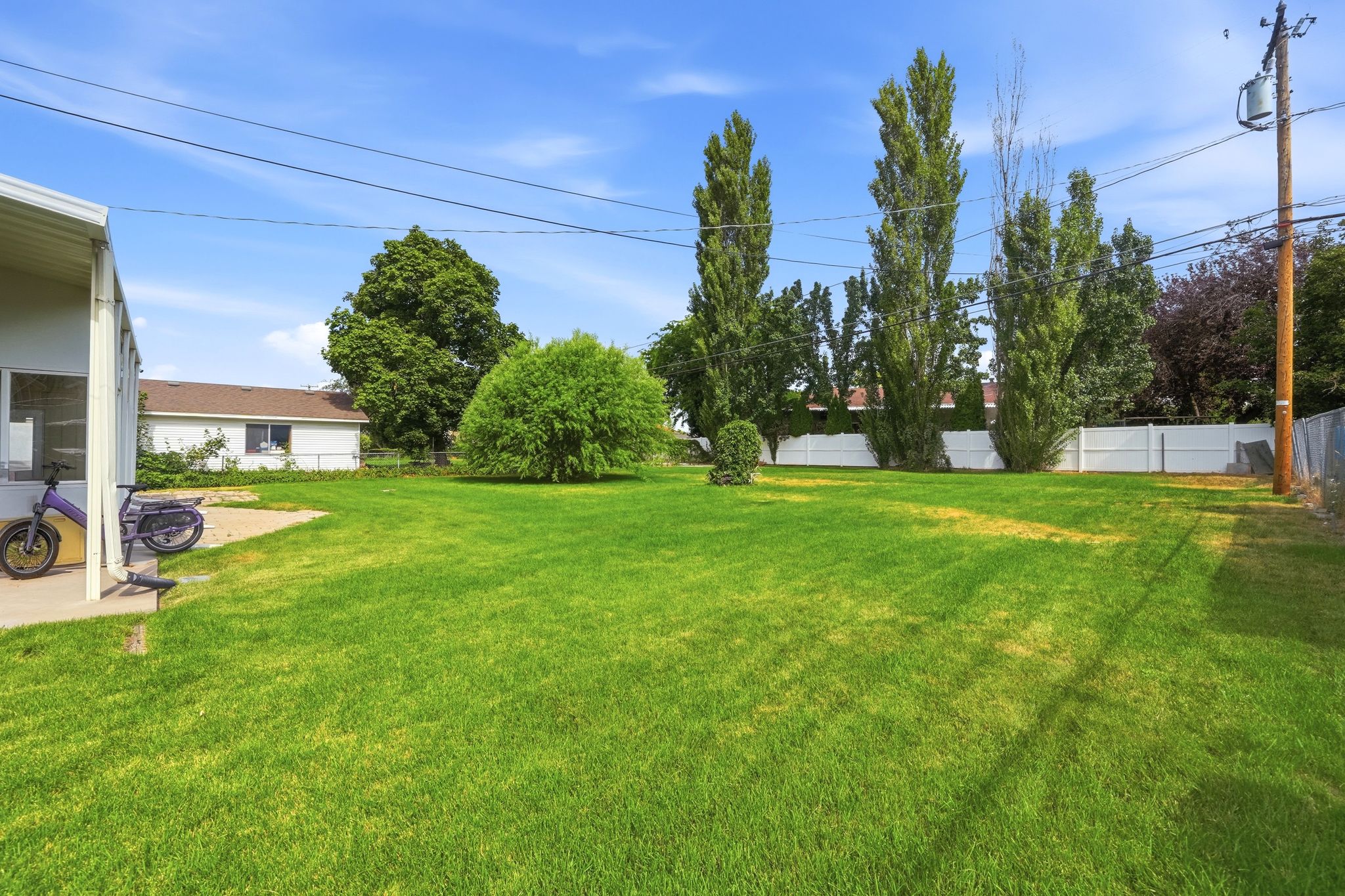 Expansive green lawn with mature trees and a white privacy fence