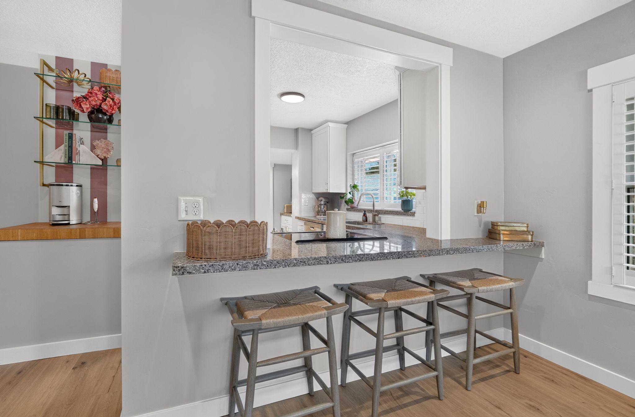 Kitchen pass-through featuring a granite countertop with seating, white shaker cabinetry, and a stainless steel sink