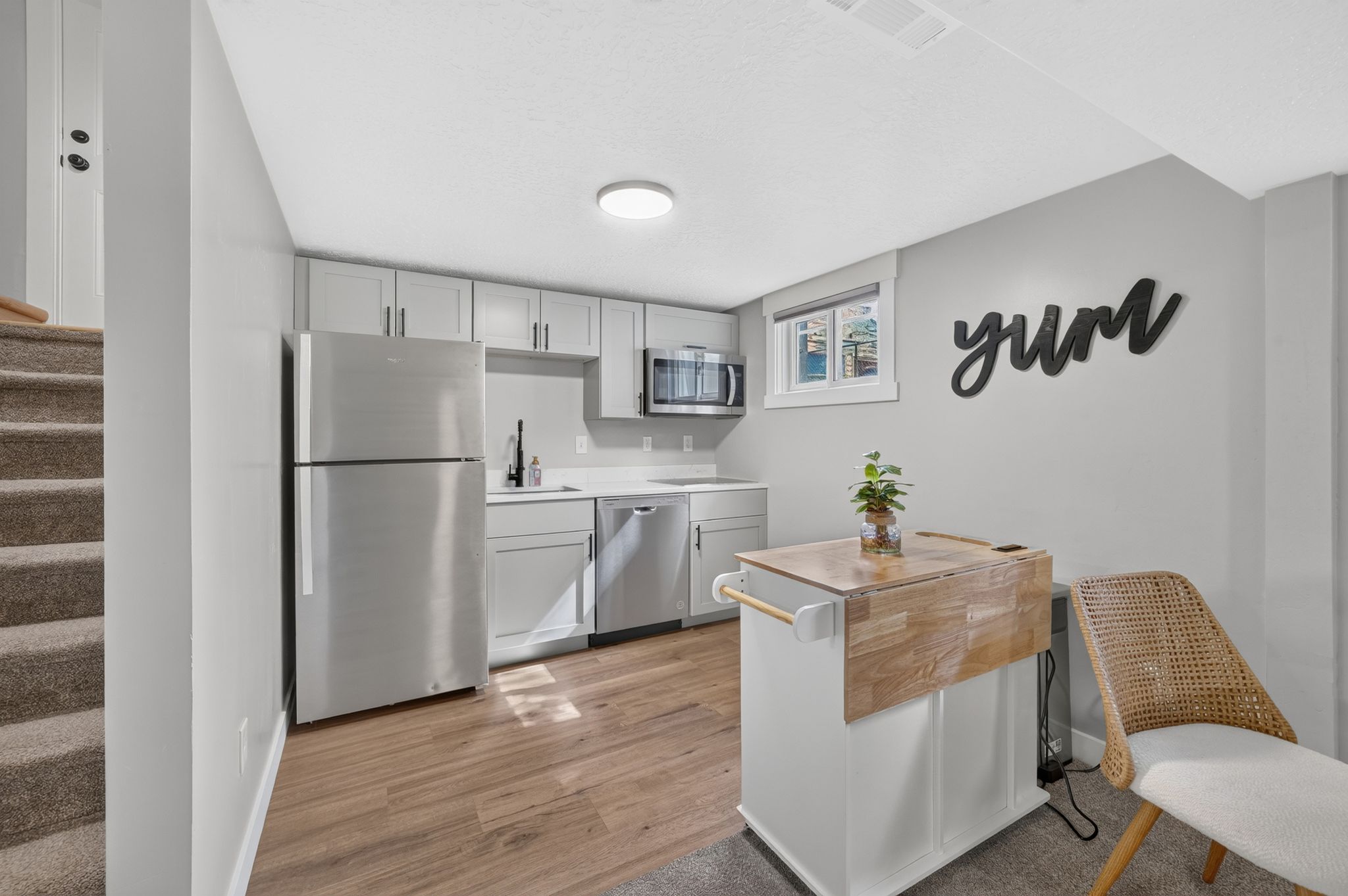 Compact kitchen featuring wood-finish flooring, light grey cabinetry, stainless steel appliances, a white countertop, and a window