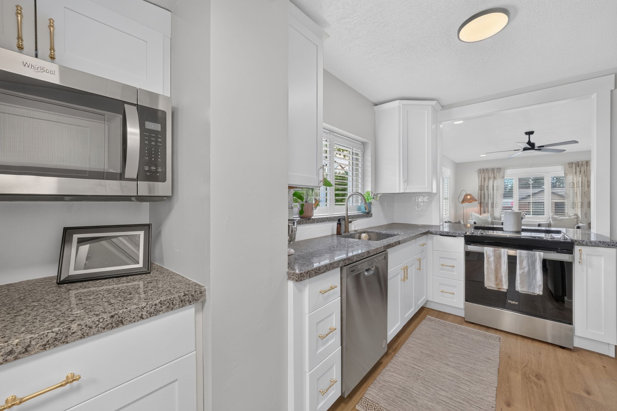 Modern kitchen featuring white cabinetry with gold-tone hardware, stainless steel appliances, speckled countertops, and wood-finish flooring