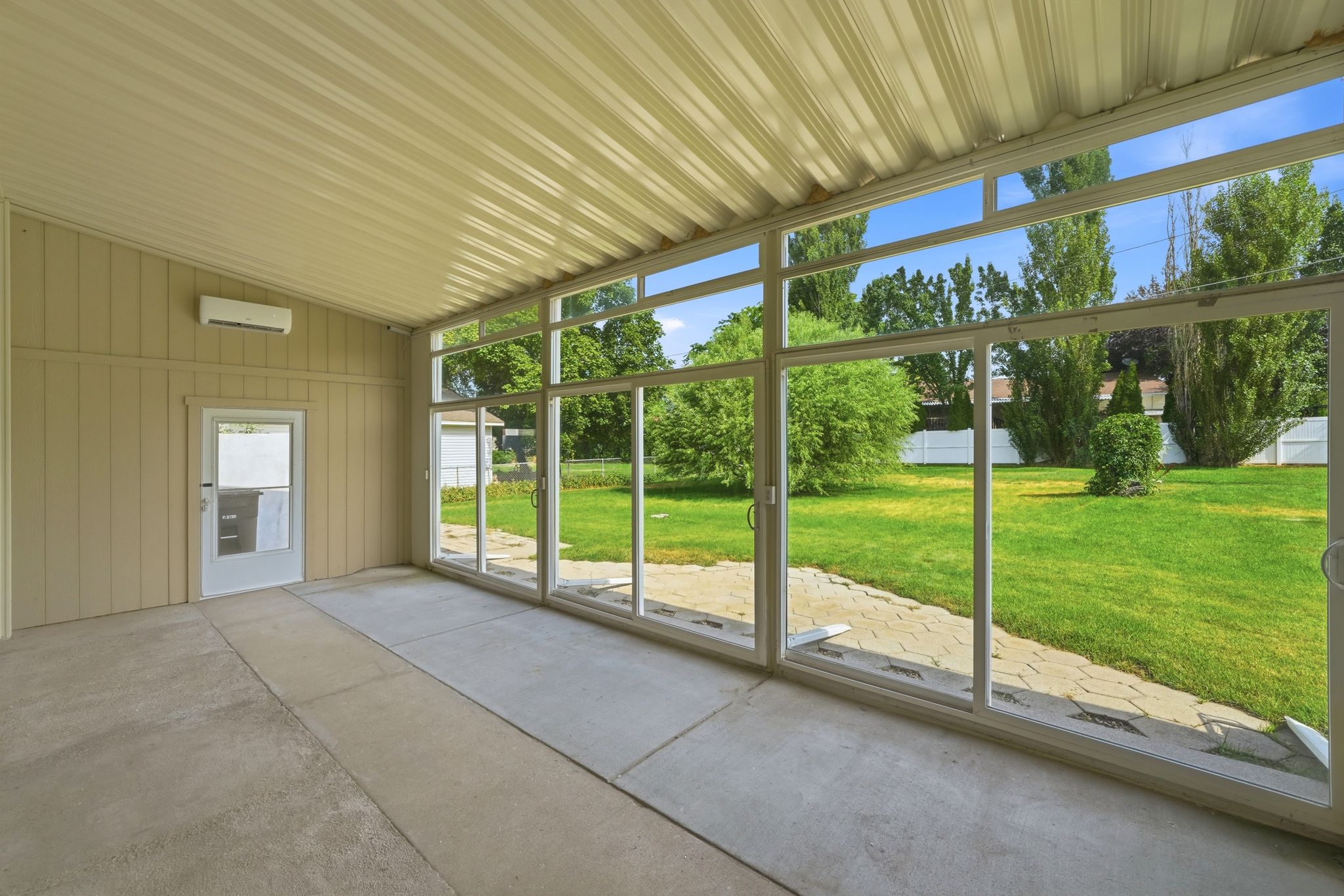 Enclosed patio featuring floor-to-ceiling glass sliding doors, concrete flooring, and a corrugated metal ceiling