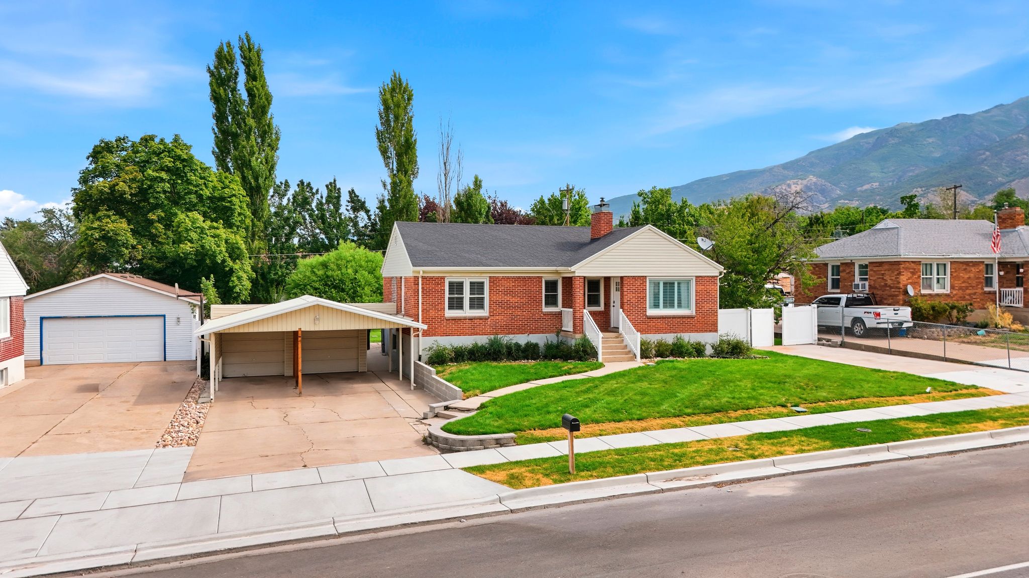 Brick exterior residence featuring a front lawn with mature landscaping, a two-car carport, a separate detached garage, and a concrete driveway