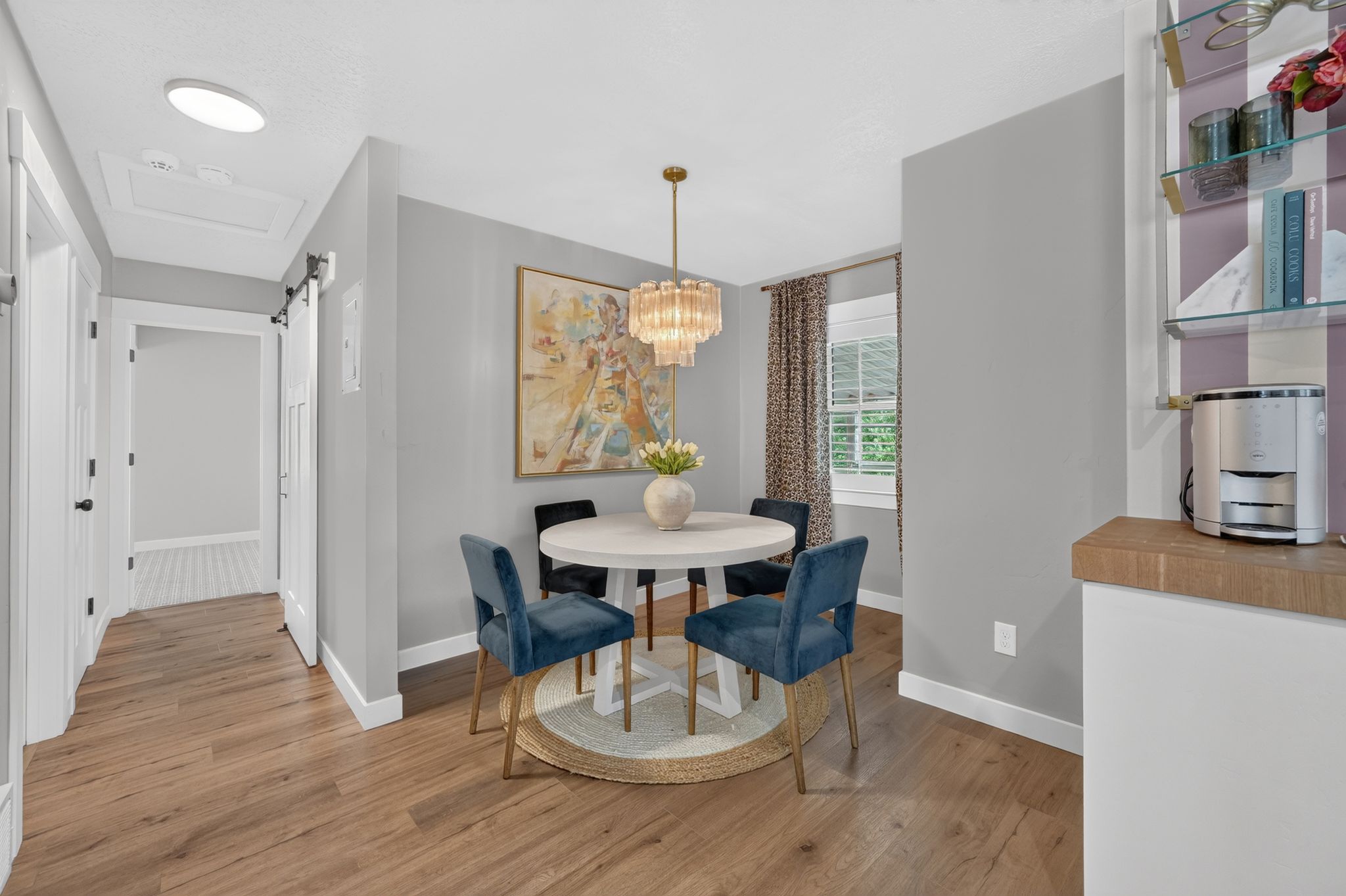 Open dining area featuring wood-finish flooring, a contemporary chandelier, and a large window with patterned drapes