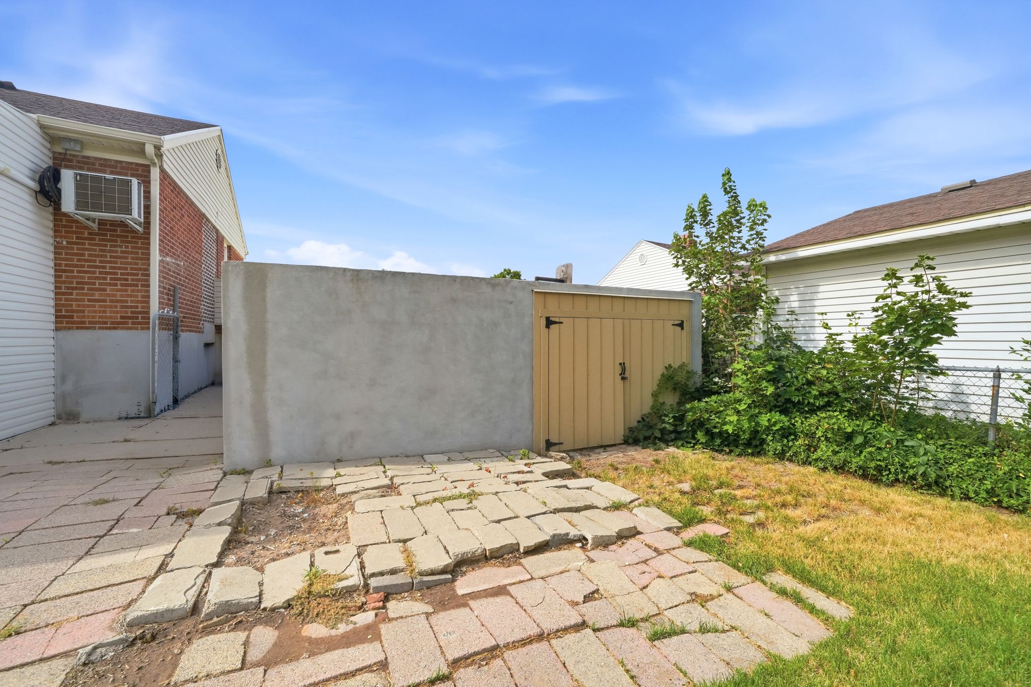 Outdoor area featuring a paved brick patio, a concrete privacy wall, and a wooden storage shed with black hardware