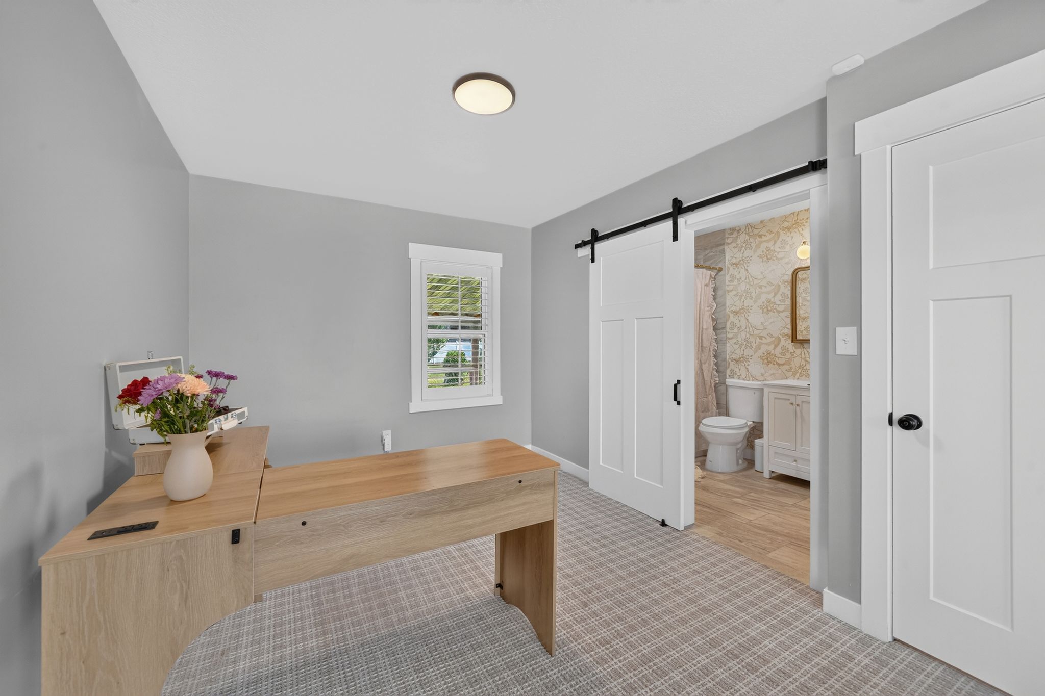Room featuring light gray wall paint, patterned carpet flooring, and a white barn door with black hardware opening to a bathroom