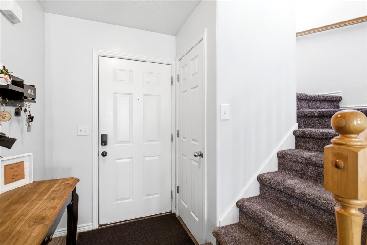 Entryway featuring a paneled door with smart lock hardware, hardwood-finish flooring, and a carpeted staircase with a light wood newel post