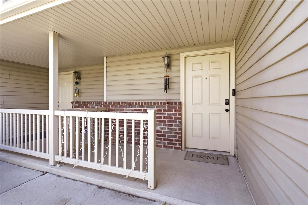 Covered porch featuring a paneled entry door, brick wainscoting, and beige siding