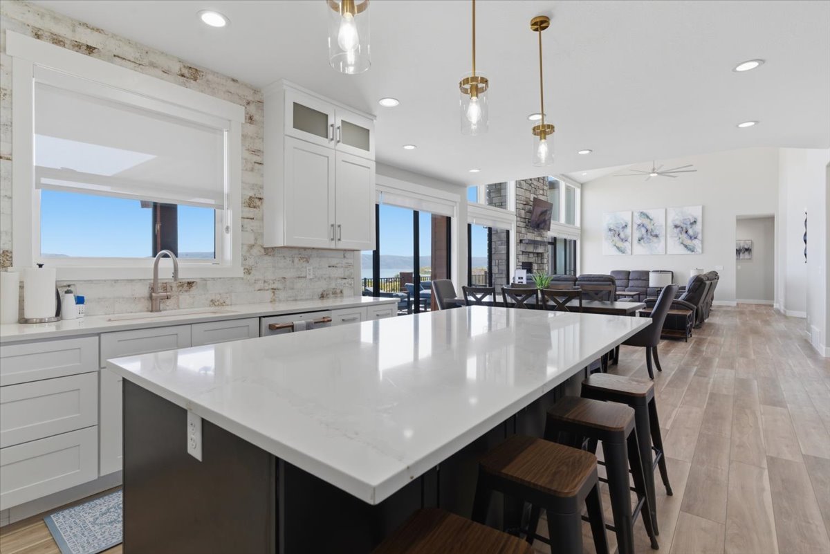 Open-concept kitchen and living area featuring a large center island with seating, white shaker cabinetry, and light-toned wood-finish flooring