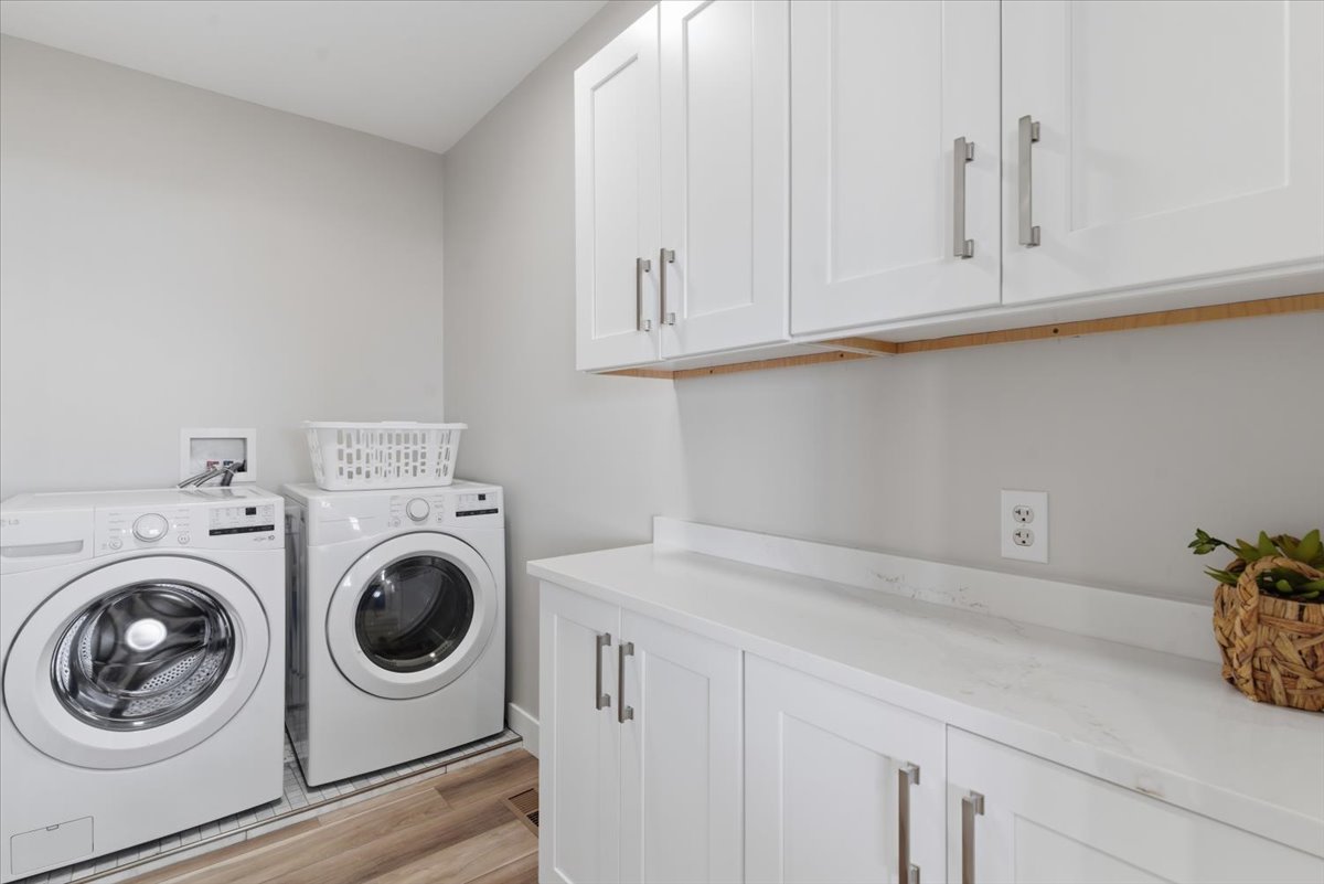 Laundry area featuring white shaker-style cabinetry, a light-toned countertop, and wood-finish flooring