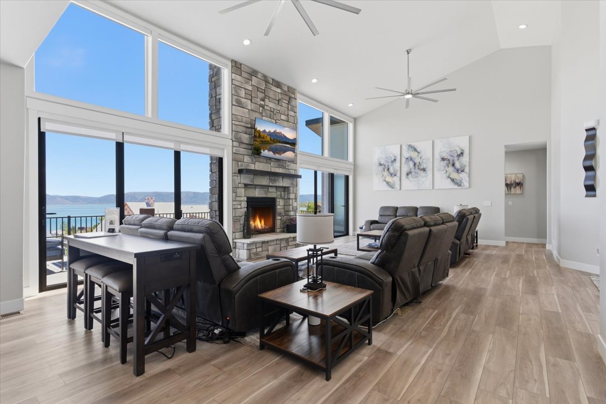 Vaulted ceiling living area featuring a stone fireplace, large format tile flooring, contemporary ceiling fans, and expansive windows with water scenery