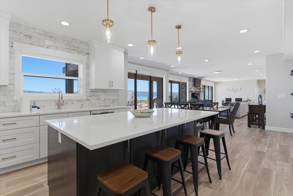 Contemporary kitchen featuring a large central island with a solid surface countertop, brass-finish pendant lighting, white upper and lower cabinetry, and a full-height stacked stone backsplash