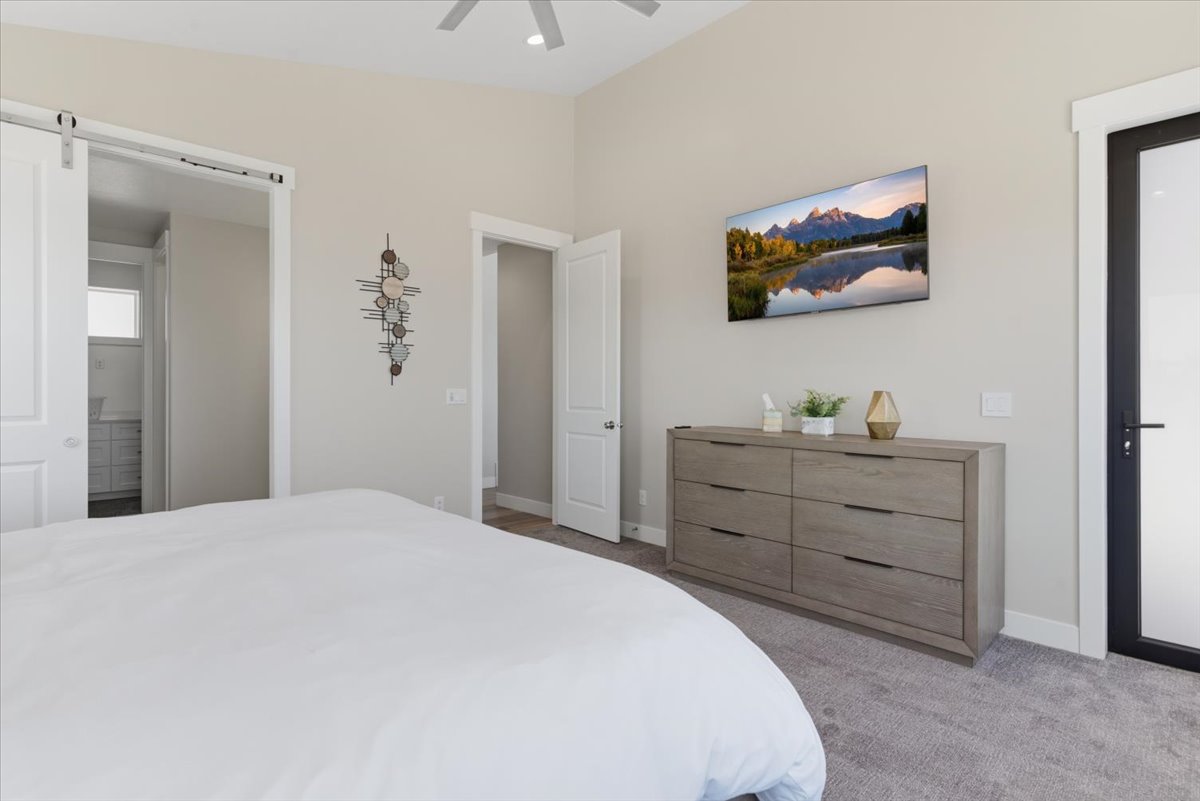 Carpeted bedroom featuring vaulted ceilings, a ceiling fan, and a barn door entry to an adjacent space