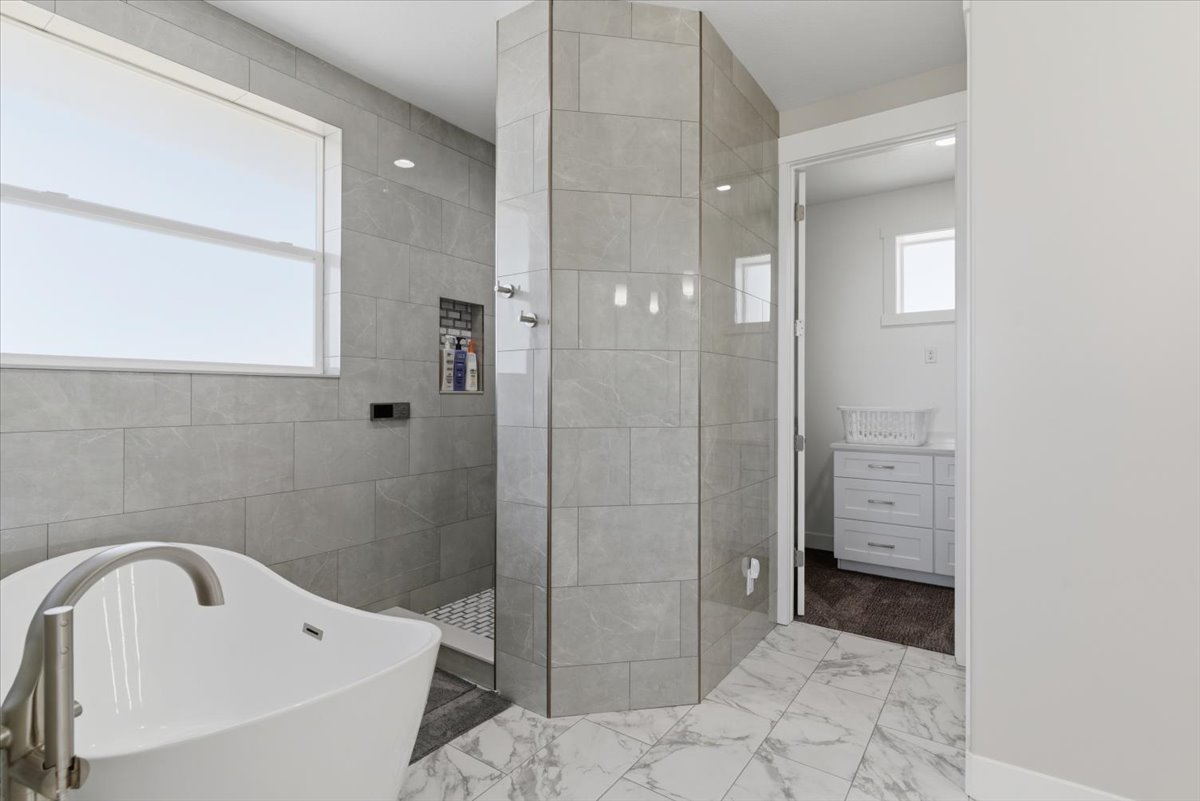 Freestanding soaking tub with a brushed nickel faucet, large format tile flooring, and a walk-in shower with built-in niche and multiple shower heads