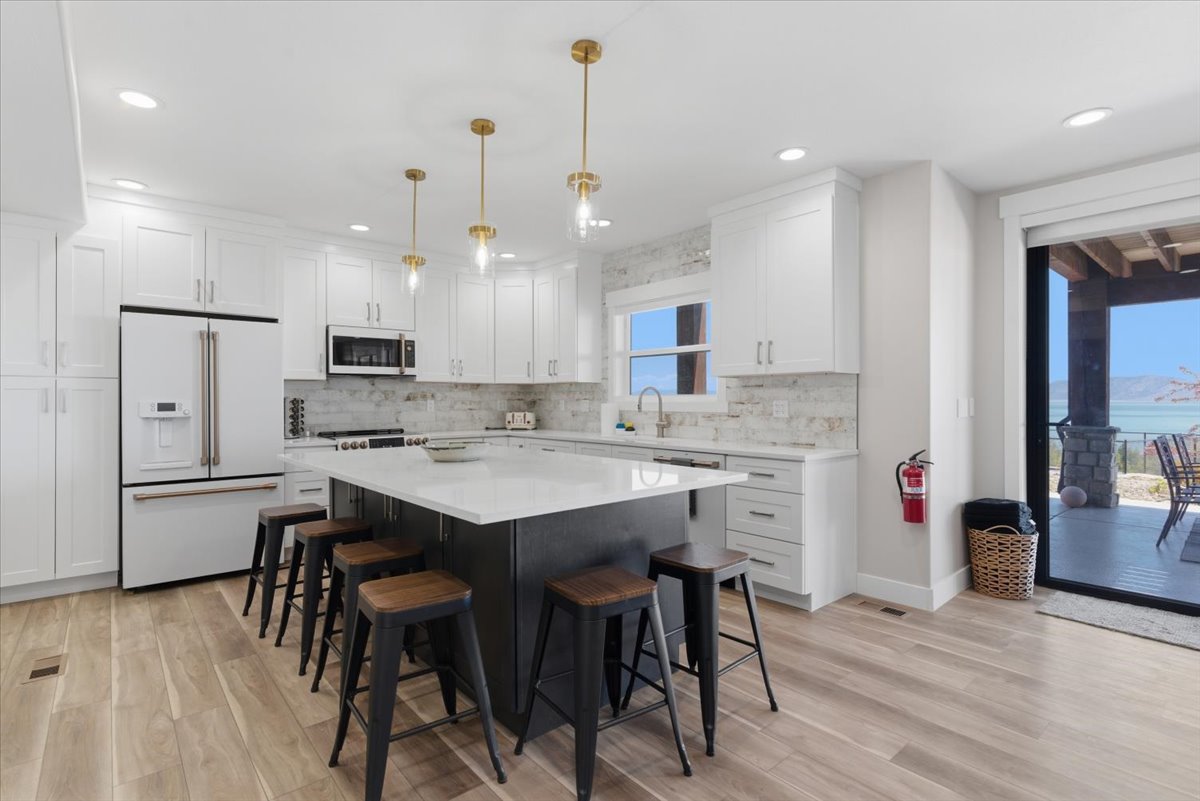 White kitchen featuring a dark island with seating, pendant lighting, built-in appliances, and wood-finish flooring