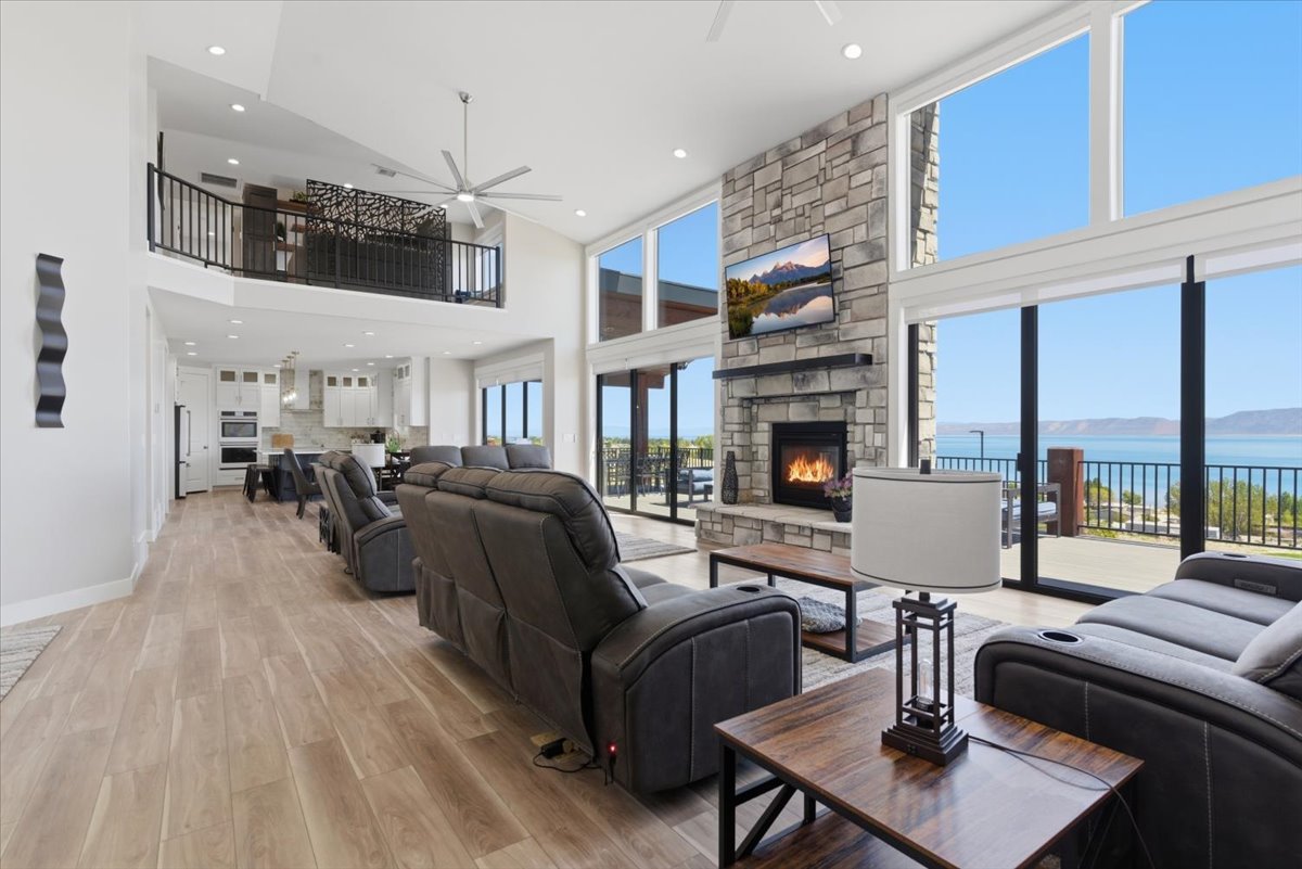Open-concept living area featuring a stone-clad fireplace with a hearth, wood-finish flooring, and expansive windows