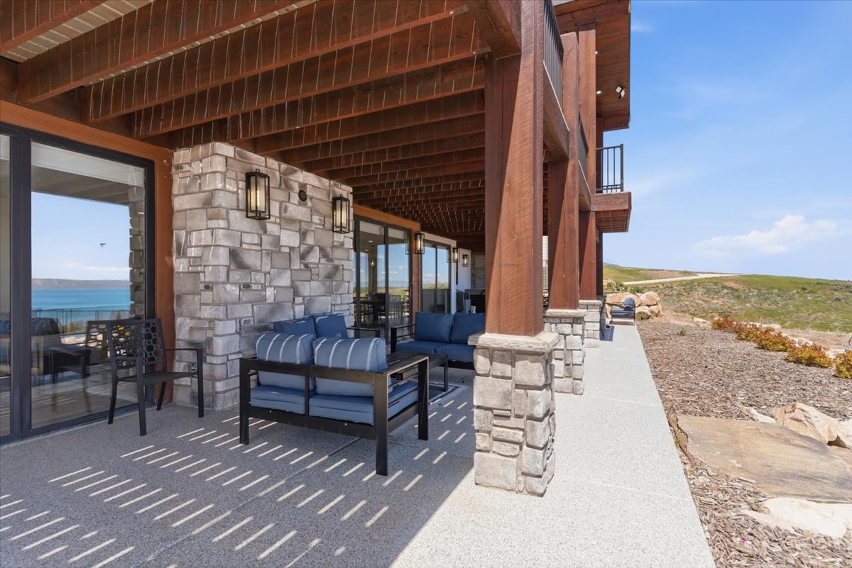 Expansive outdoor patio featuring a stone veneer wall, multiple large glass sliding doors, stone-clad structural columns, and a finished ceiling