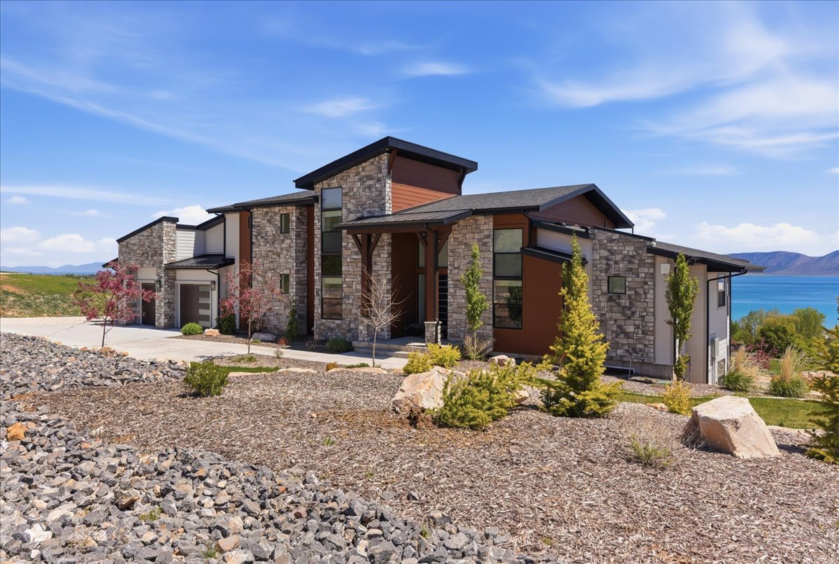 Contemporary multi-level residence featuring stone and wood siding, a multi-car garage, and a covered entry