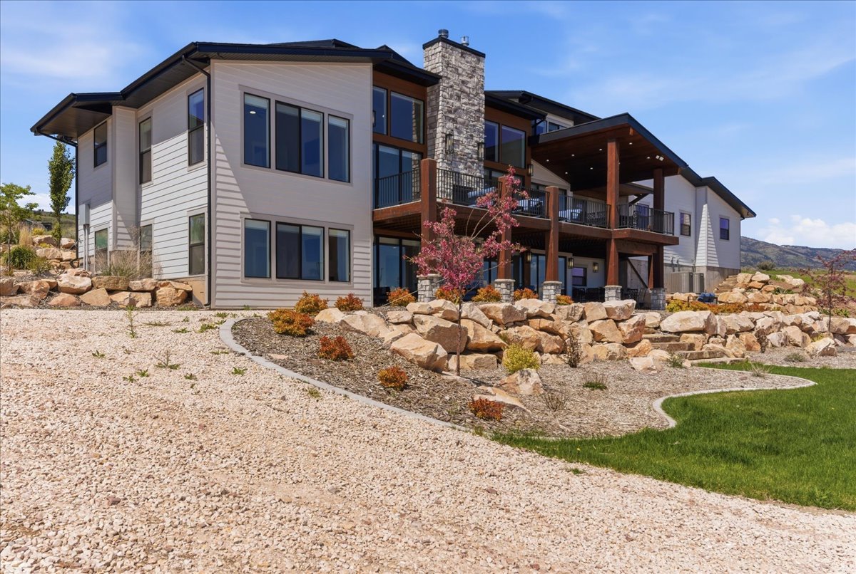 Modern multi-level exterior featuring light-colored siding, a prominent stone chimney, and expansive windows