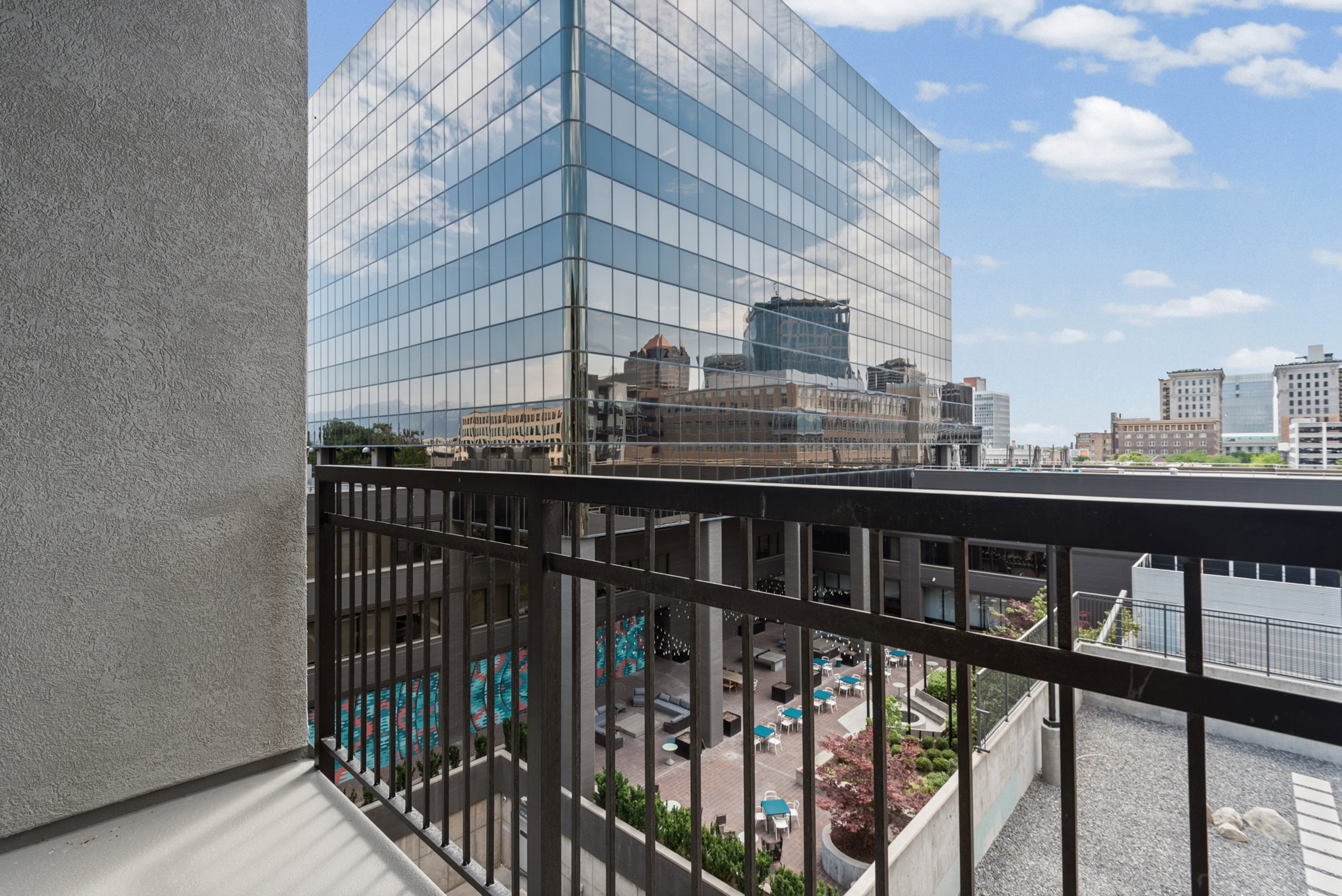 Balcony with metal railings overlooking a common area courtyard and an adjacent glass-exterior building