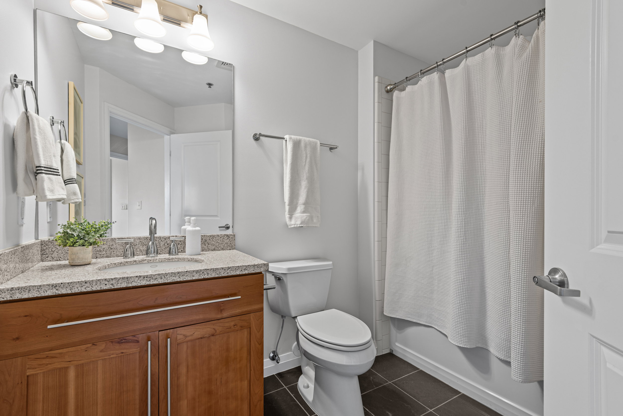 Bathroom featuring a wood-finish vanity with a light speckled countertop, an undermount sink, and a large wall-mounted mirror