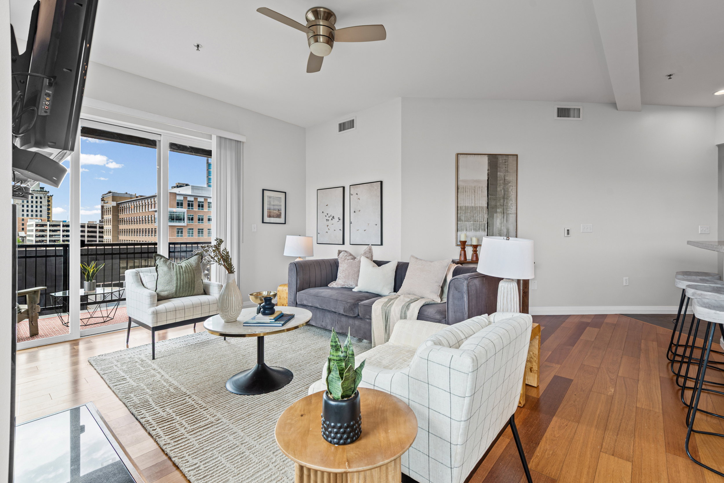 Open-concept living area featuring wood-finish flooring, a ceiling fan, and abundant natural light from the balcony's sliding glass doors