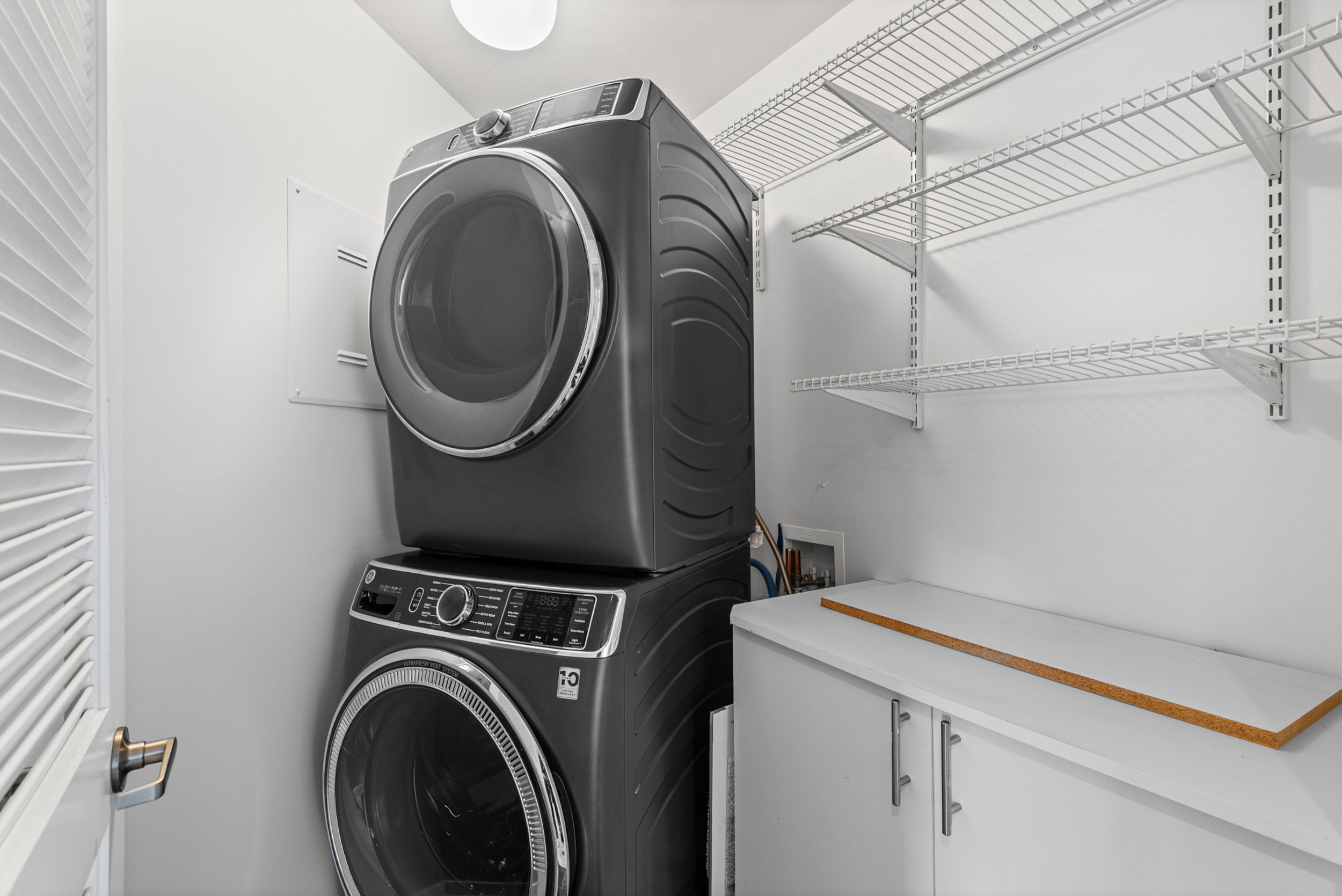 Dedicated laundry space featuring a stacked washer and dryer unit, extensive wire shelving, a built-in base cabinet, and a bright overhead light fixture