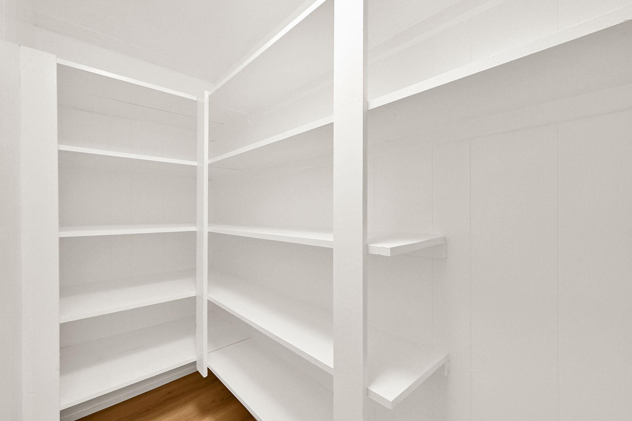 Built-in shelving system featuring multiple white shelves, a corner configuration, and wood-finish flooring