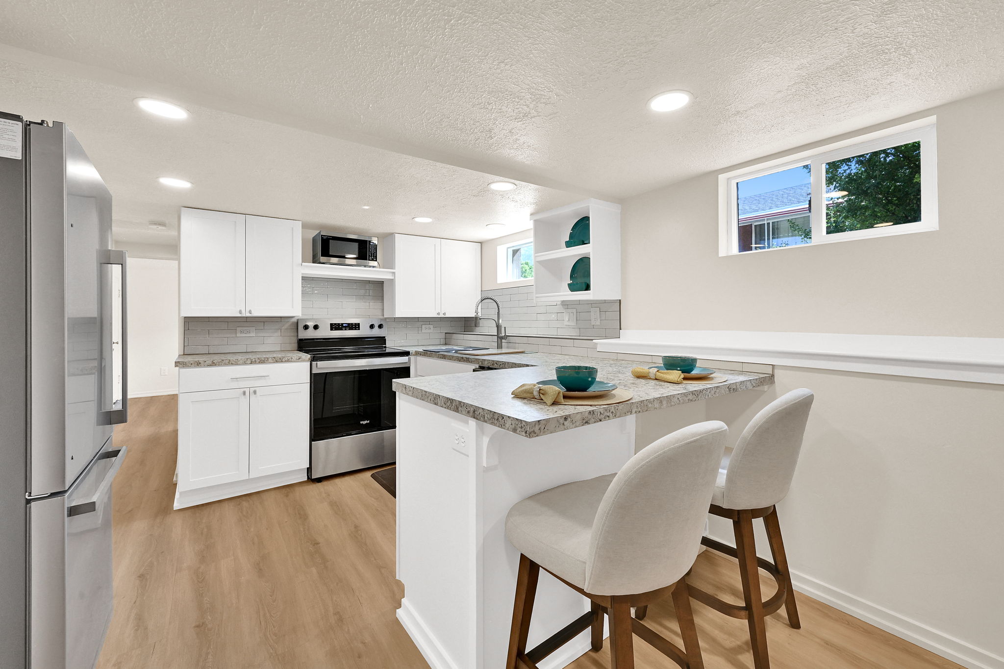 Contemporary kitchen featuring white cabinetry, stainless steel appliances, a light-toned backsplash, granite-finish countertops, and wood-finish flooring
