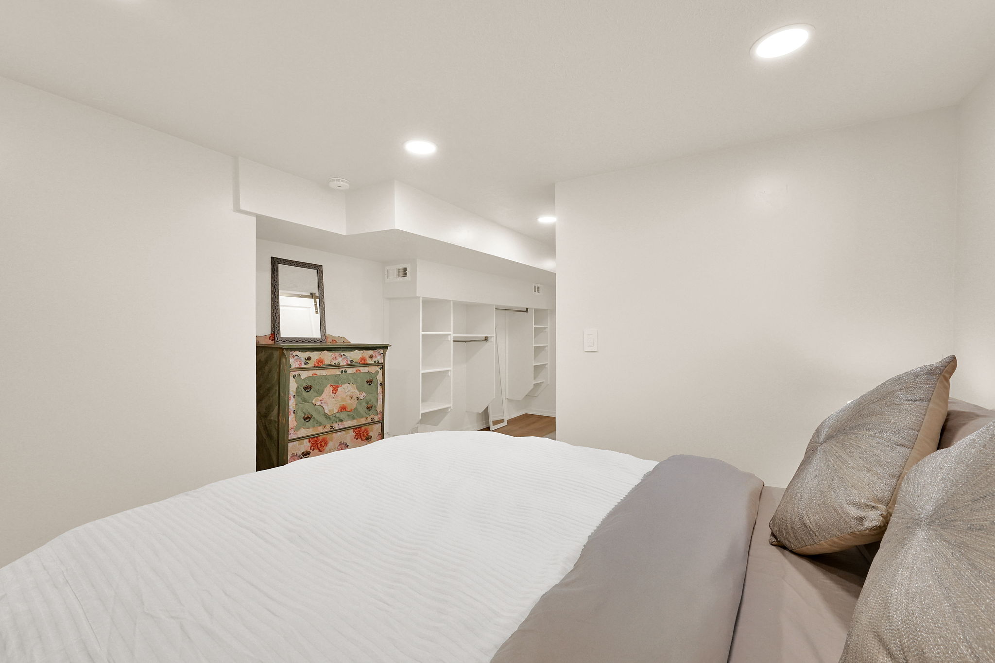 Recessed lighting illuminates a spacious room featuring a built-in closet system with open shelving and hanging space
