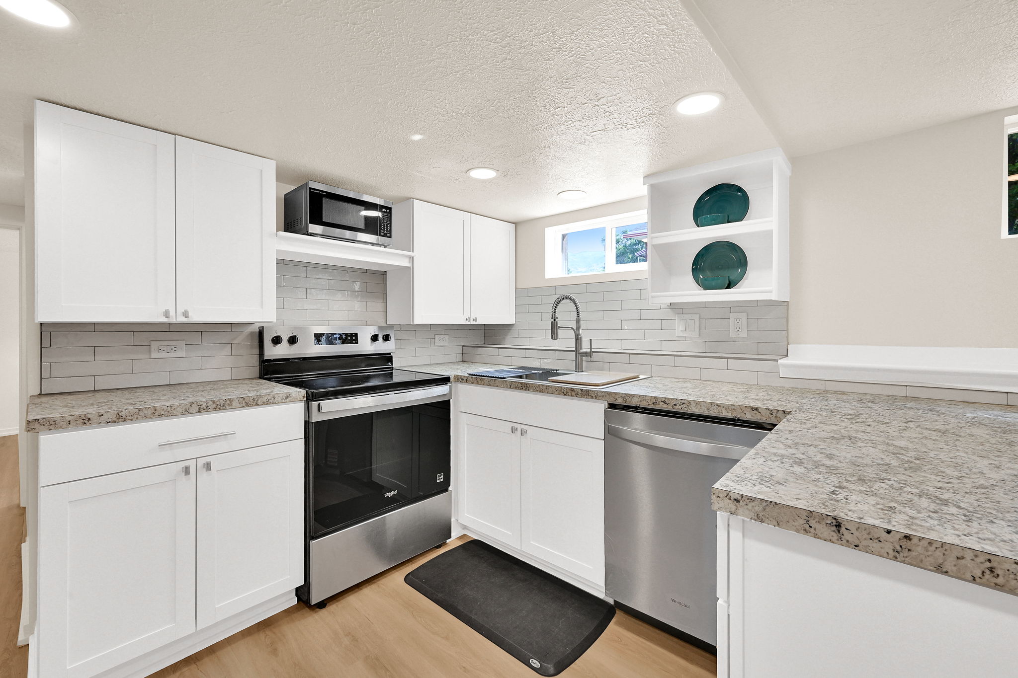 Modern kitchen featuring white shaker cabinetry, stainless steel appliances, speckled countertops, a tile backsplash, and recessed lighting
