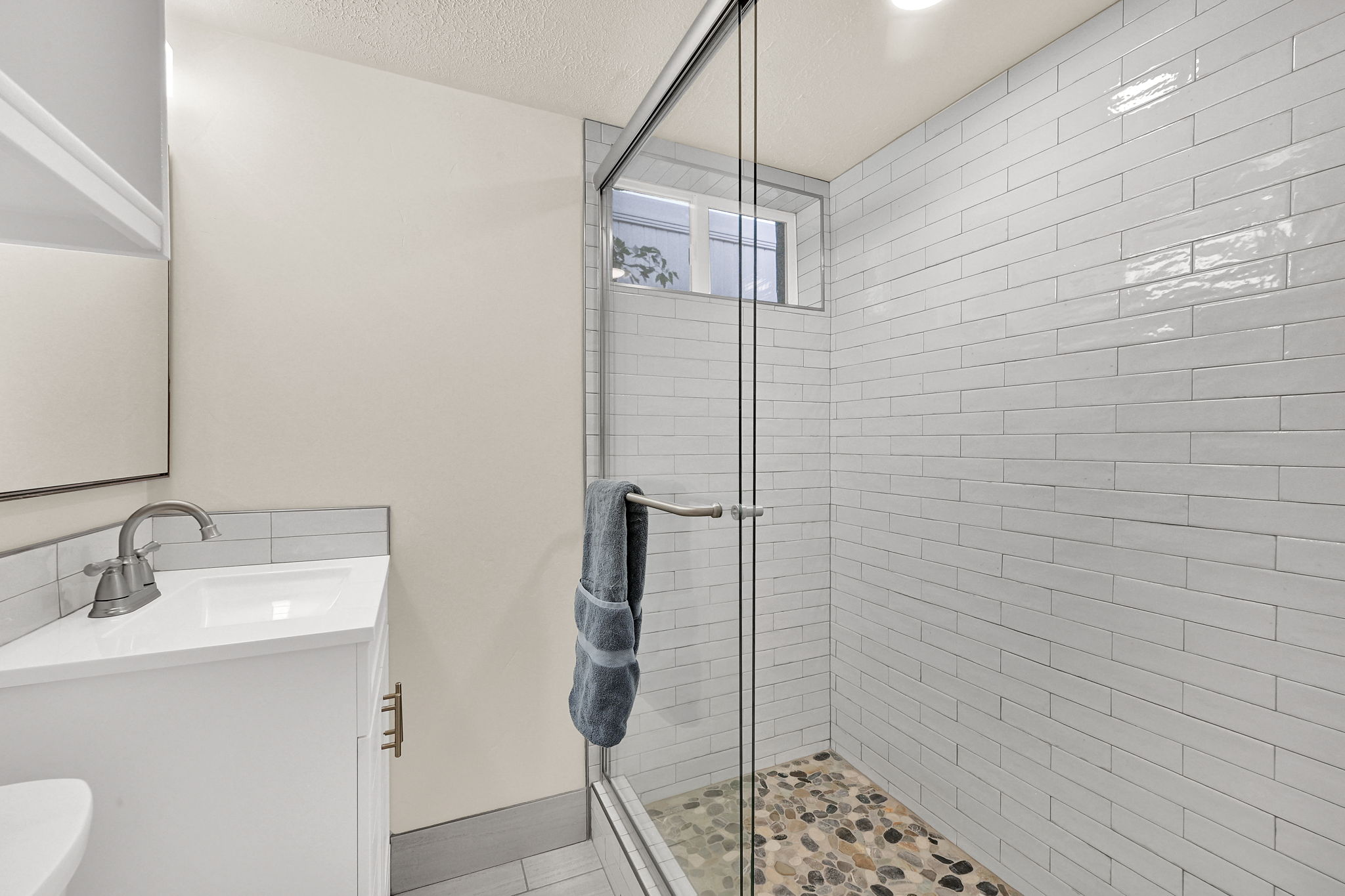Glass-enclosed shower with white subway tile surround and a pebble stone floor