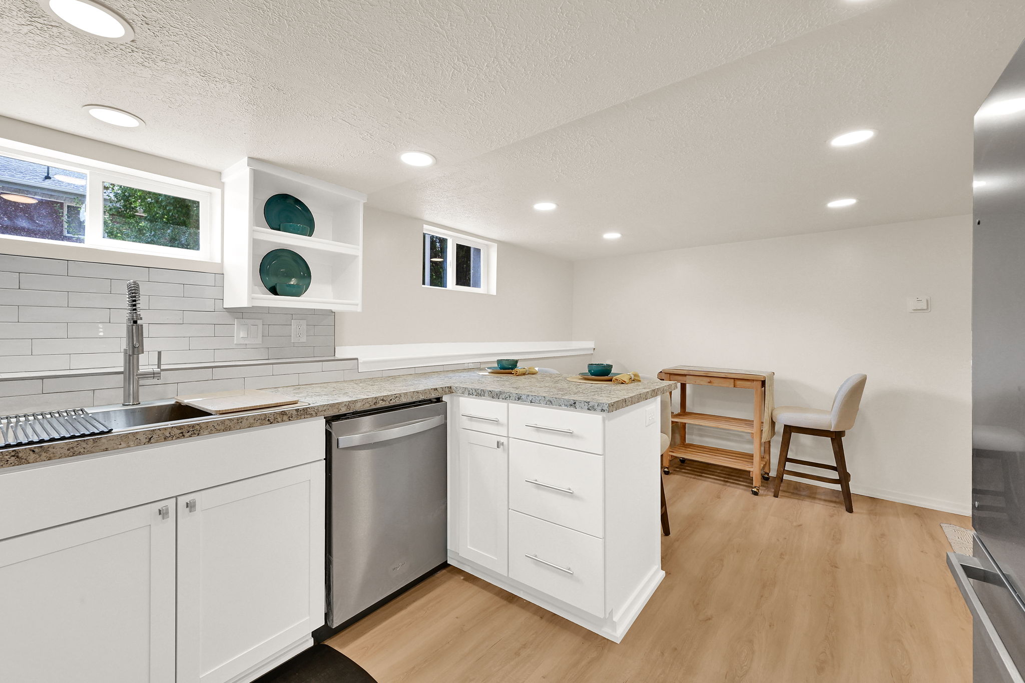 Kitchen area featuring white cabinetry, a stainless steel sink with a modern faucet, light-toned wood-finish flooring, and recessed ceiling lighting