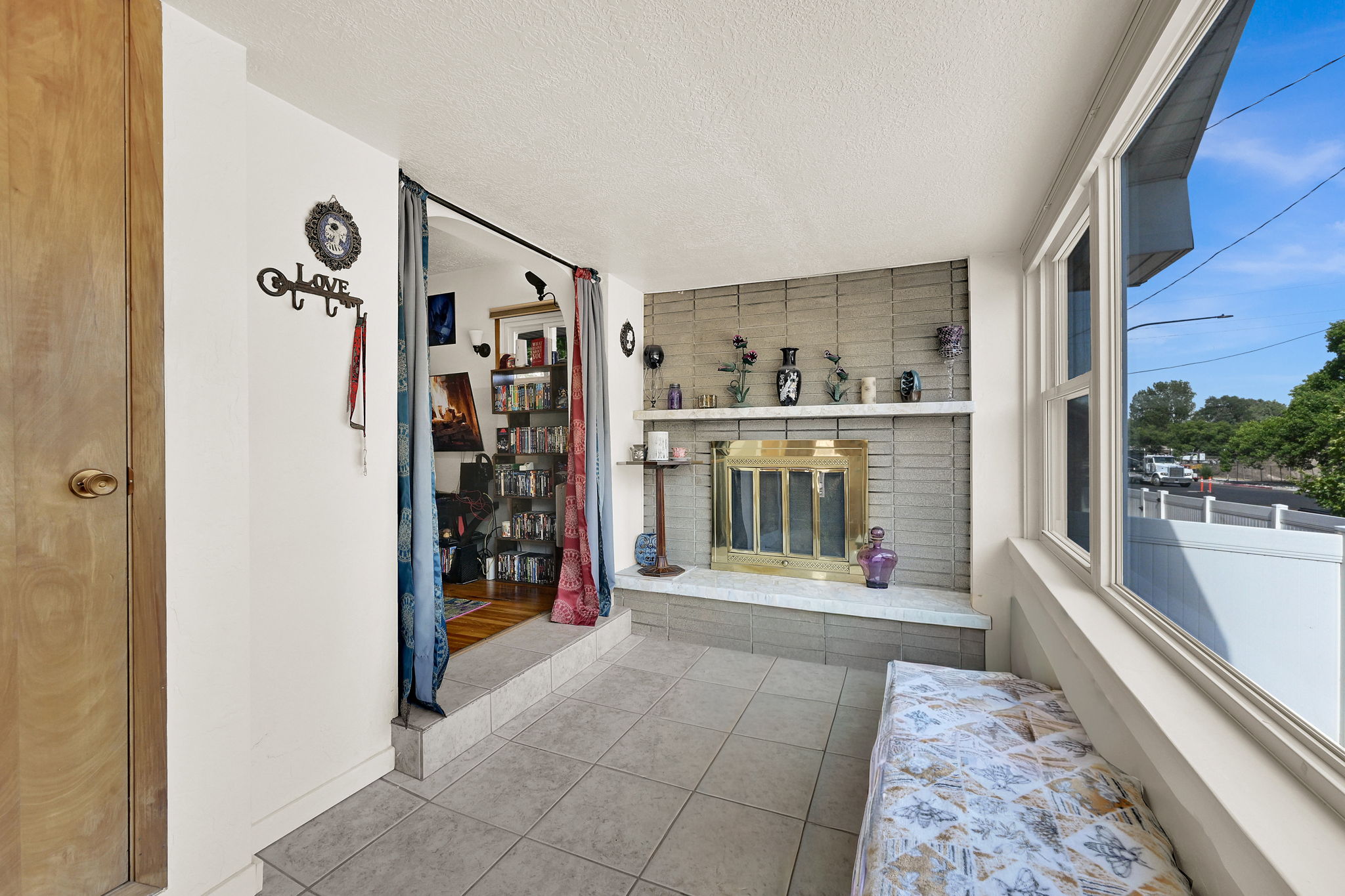 Tiled sunroom featuring large windows, a built-in fireplace with a brass-toned insert, and a white mantel